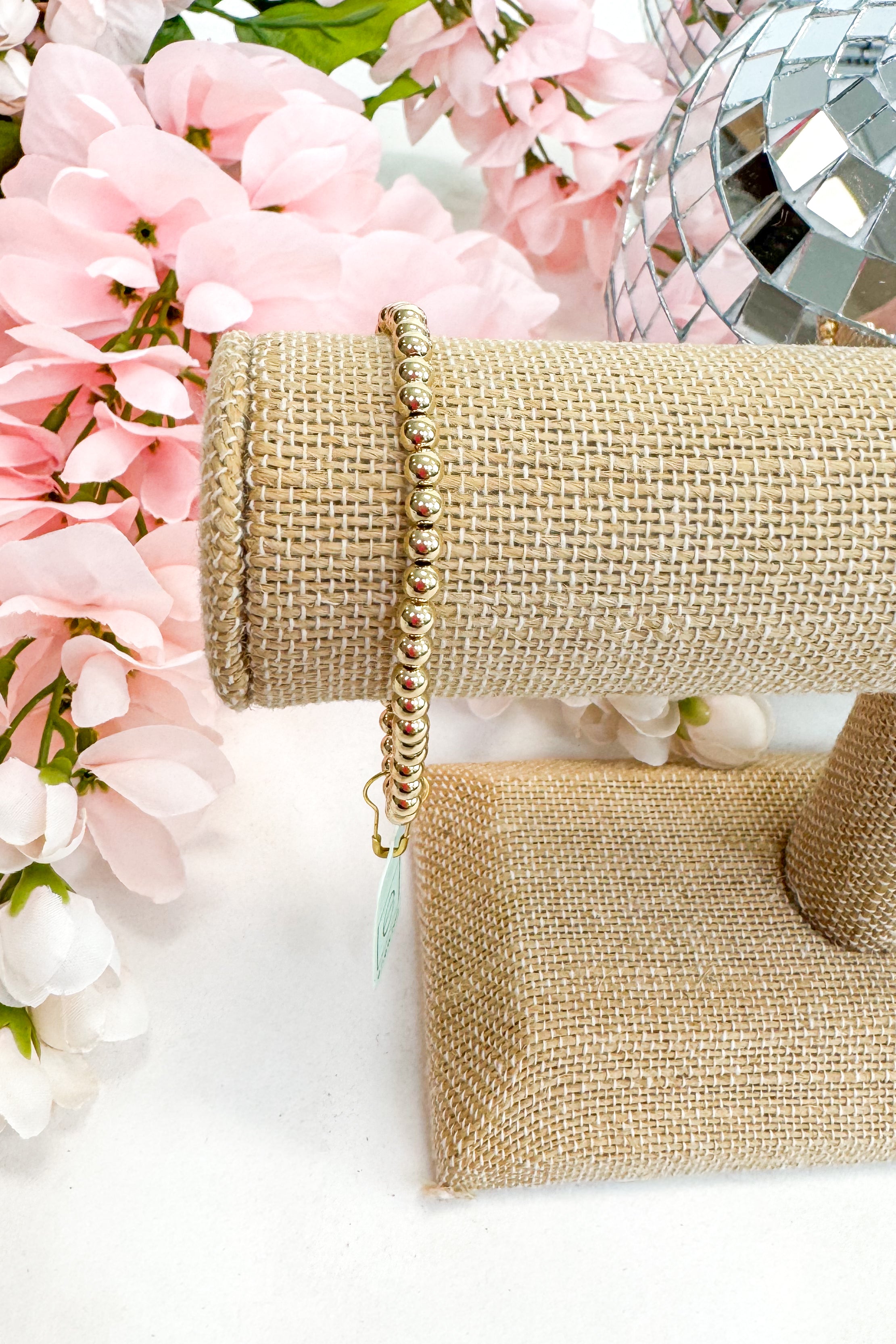 gold enewton bracelet on burlap display with flowers in background