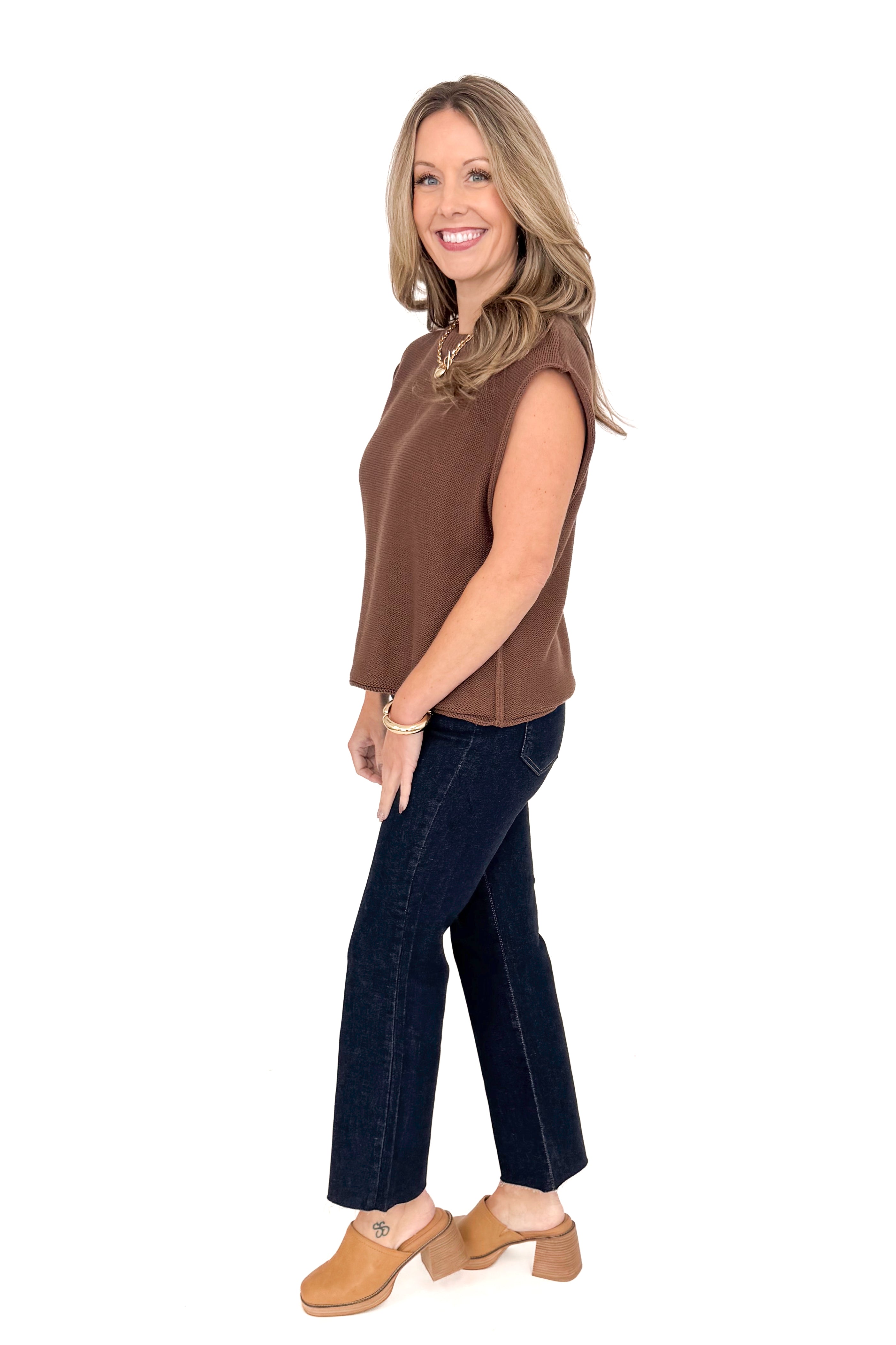 Side view of woman wearing brown sweater with jeans against white studio background.