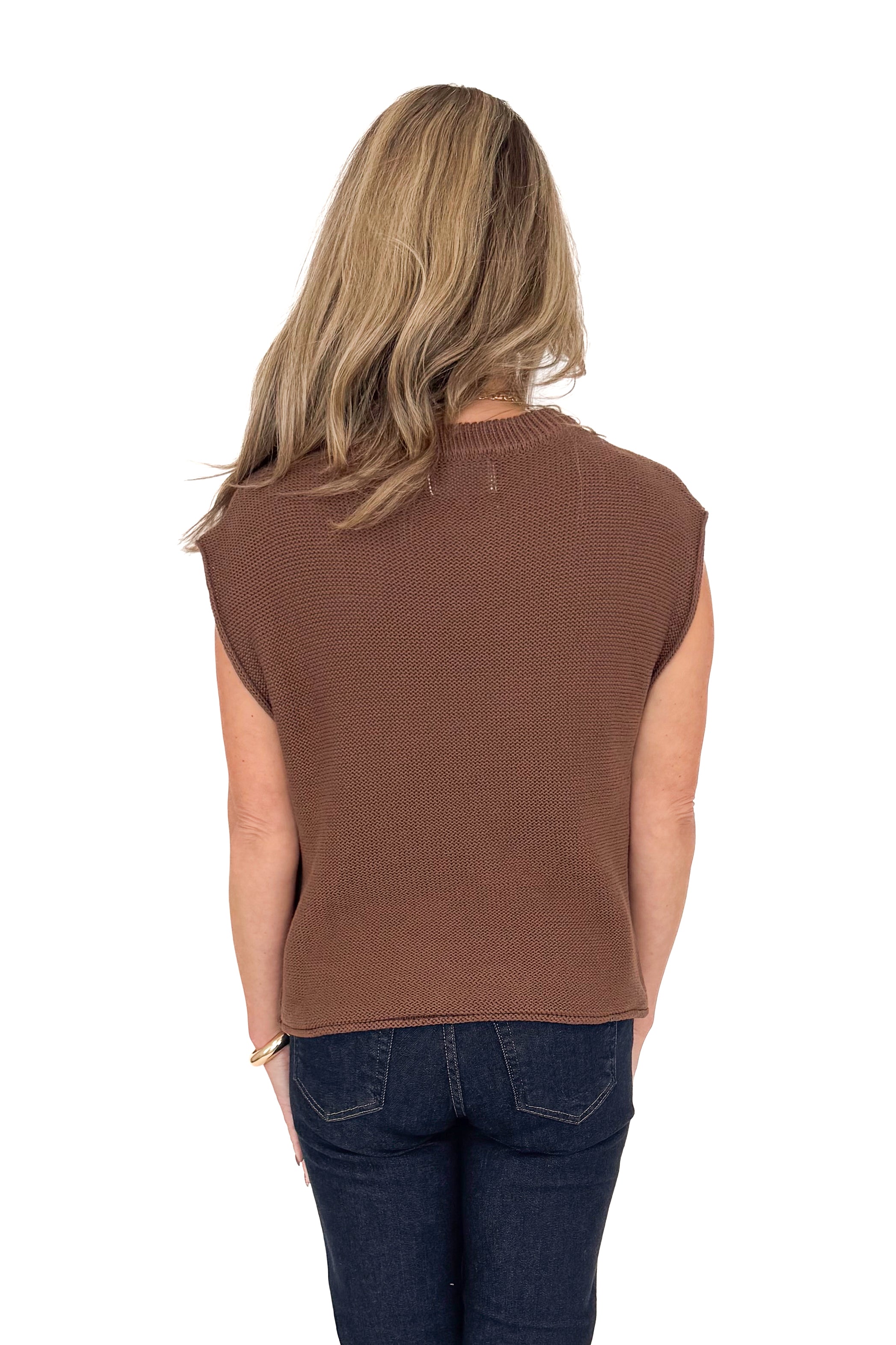 Back view of woman wearing brown sweater with jeans against white studio background.