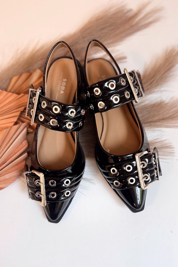Black patent leather shoes with decorative buckles on a fur surface