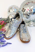 Silver sneakers with brown soles on a white surface with disco balls and flowers in the background