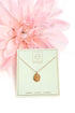Gold necklace on a green card with a pink flower in the background