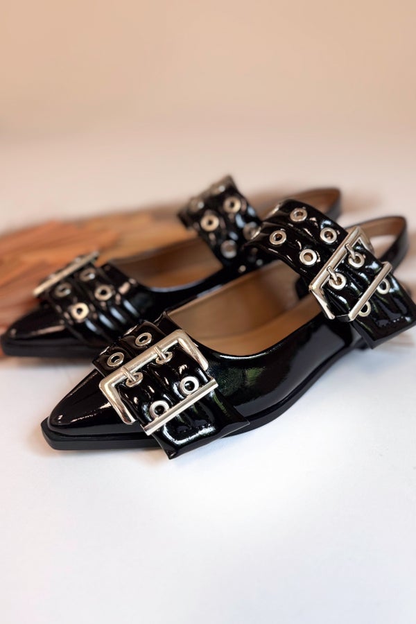 Black patent leather shoes with silver buckles on a light background