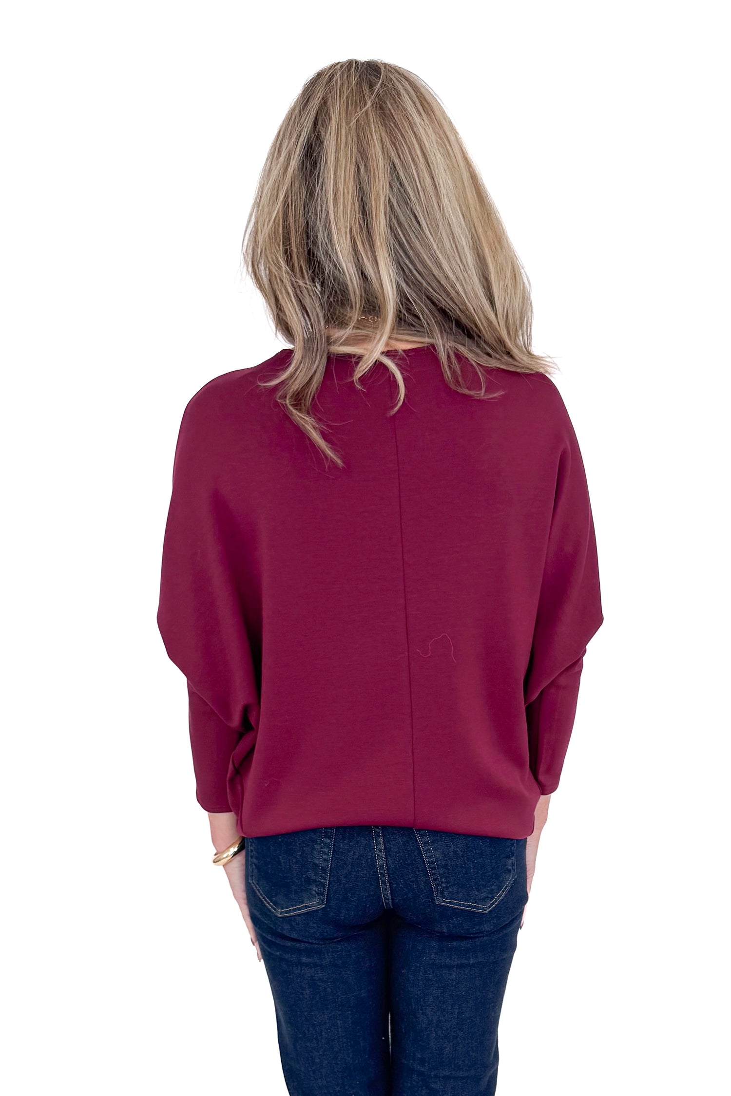 Back view of woman wearing burgundy top with jeans against white studio background.