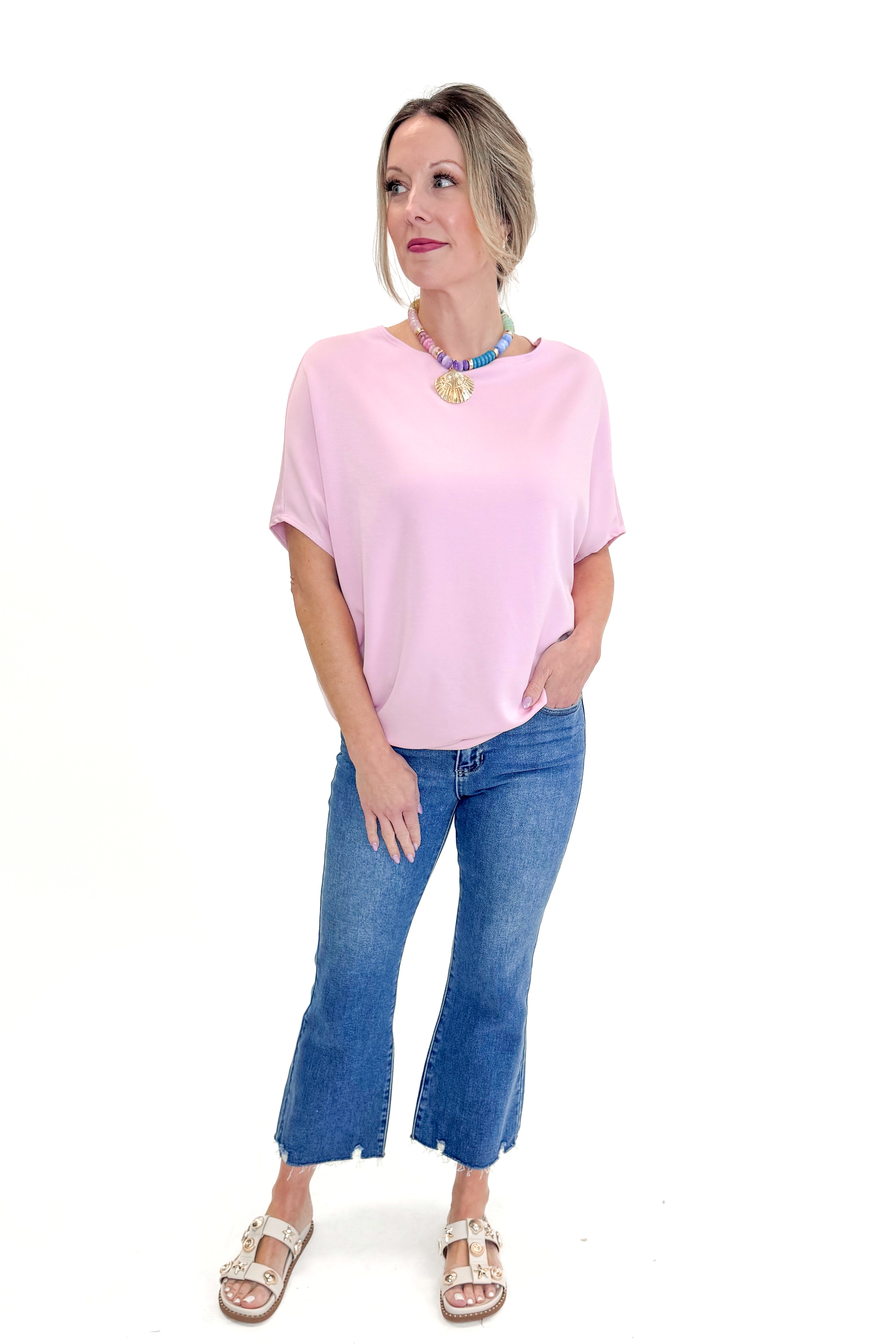 Front view of woman wearing Light Pink Dolman Sleeve Top with jeans against white studio background.