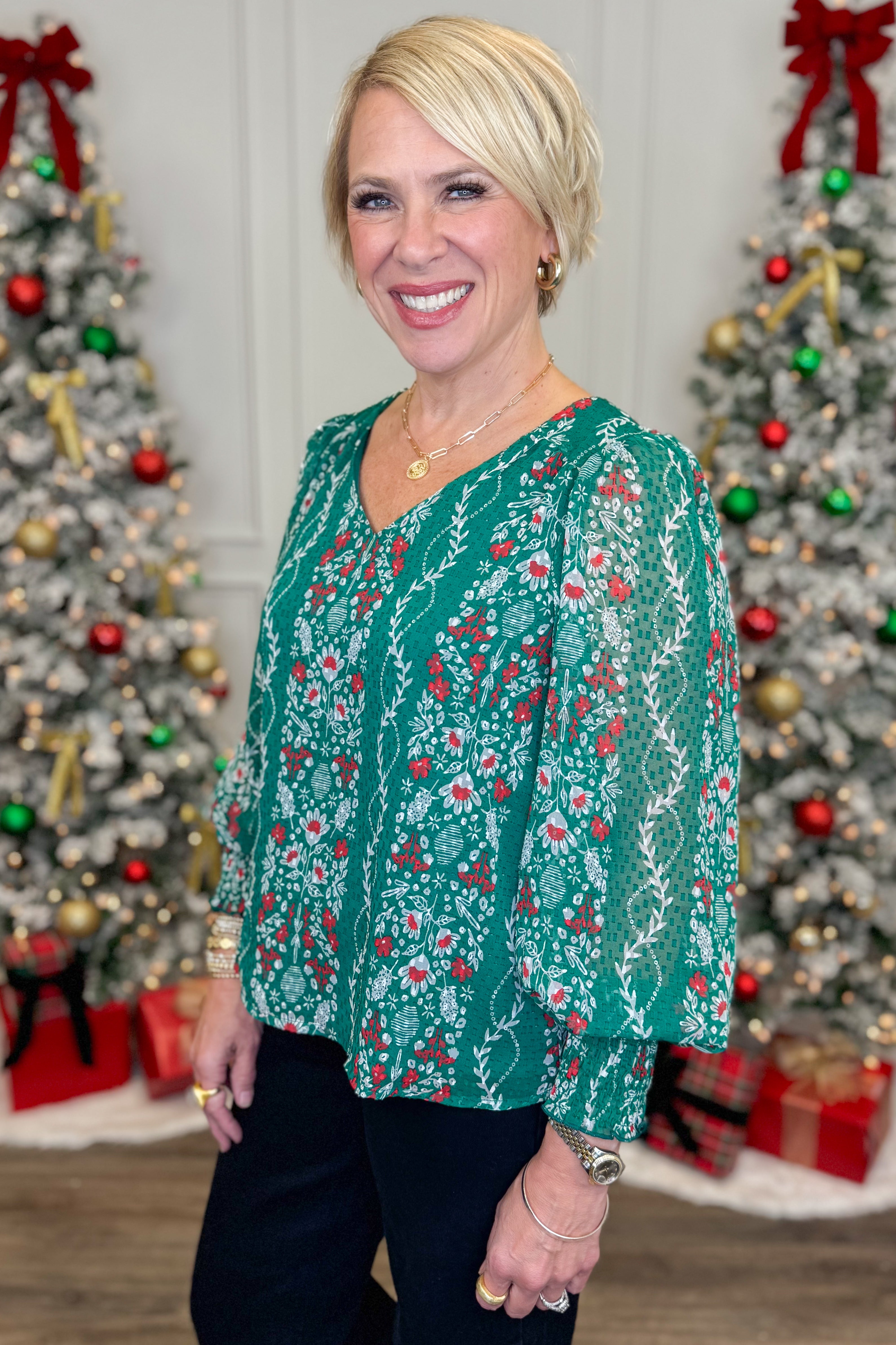 Woman wearing a green floral blouse in front of decorated Christmas trees.