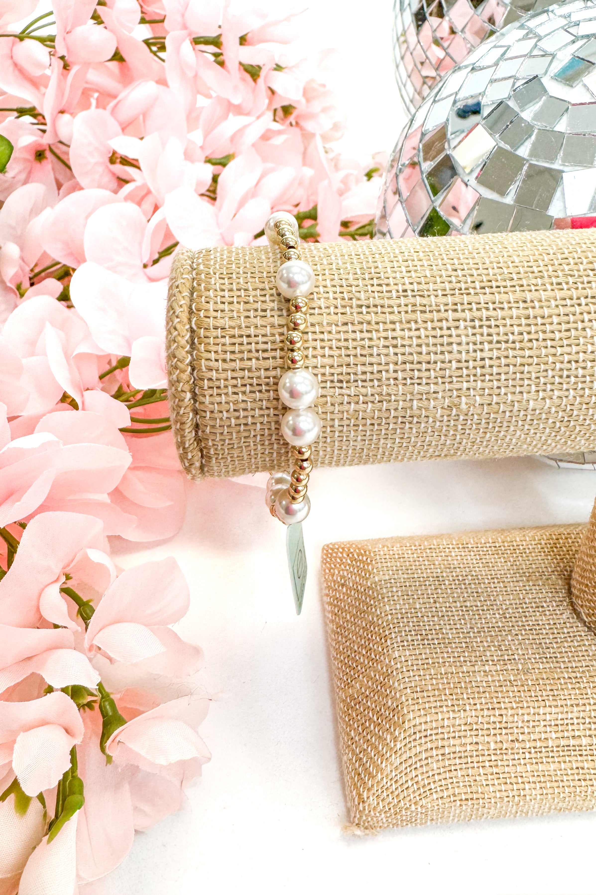 beaded bracelet with pearl detailing on a white surface with pink flowers in the background