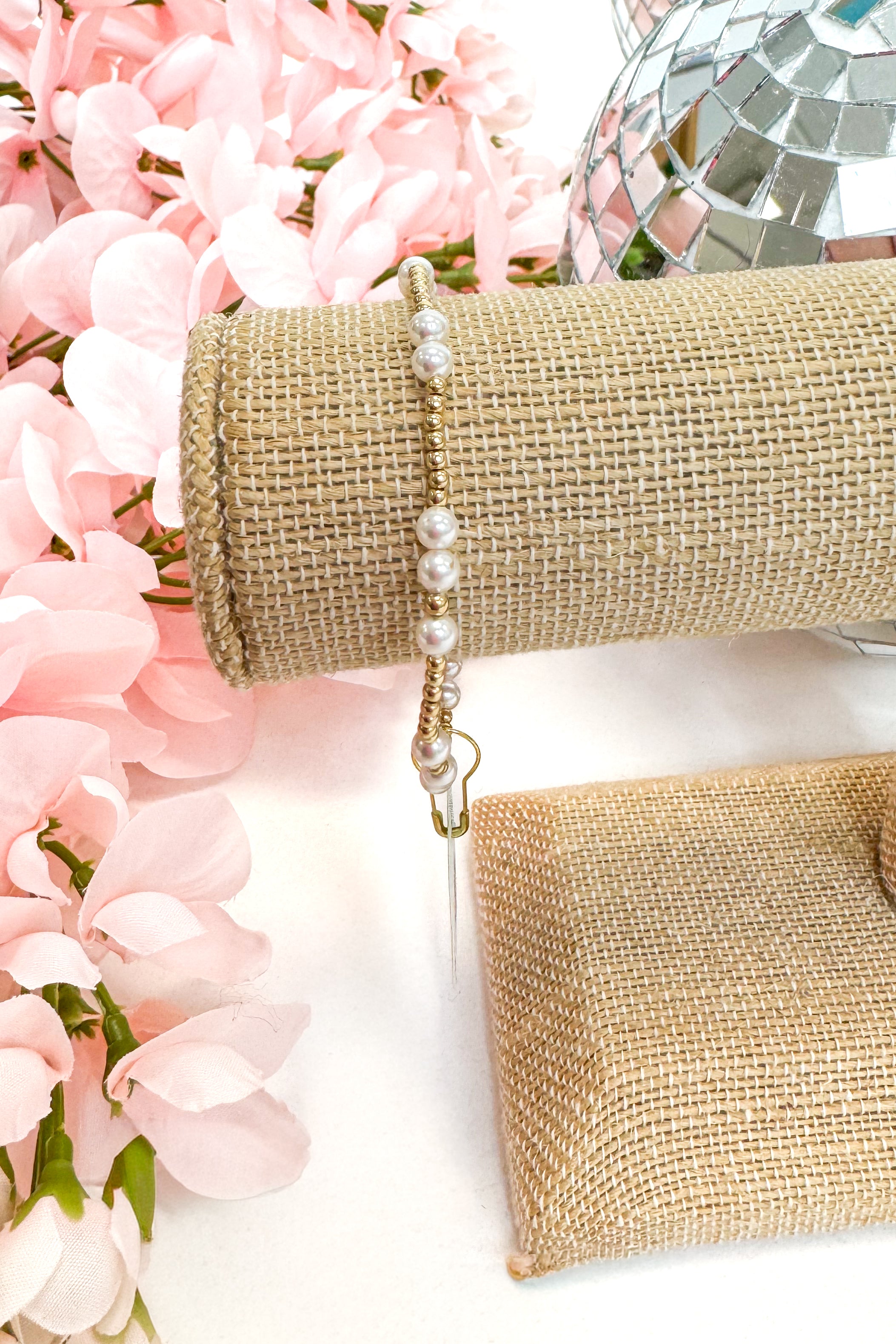 gold enewton bracelet with pearl detailing on burlap display with floral background