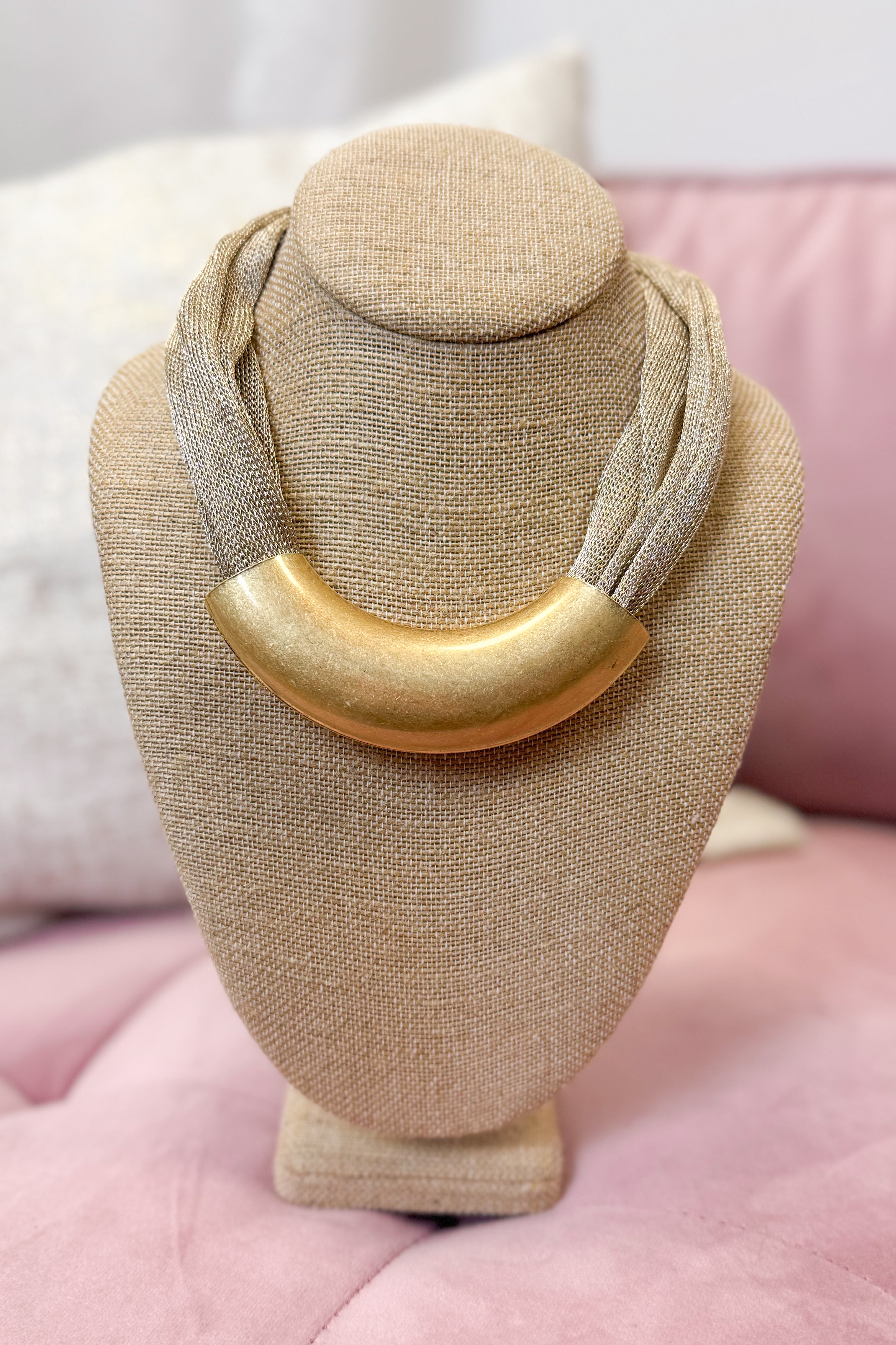 Gold necklace on a beige jewelry display stand with a pink background