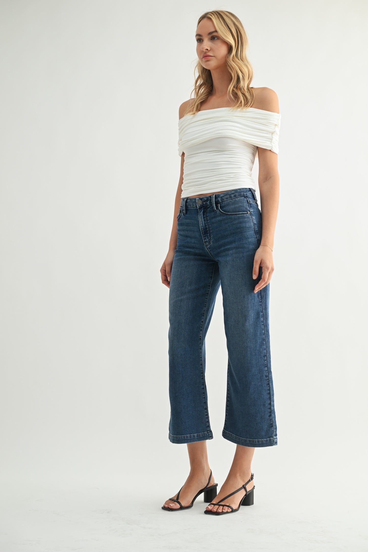 Woman wearing a white off-shoulder top and blue jeans on a white background