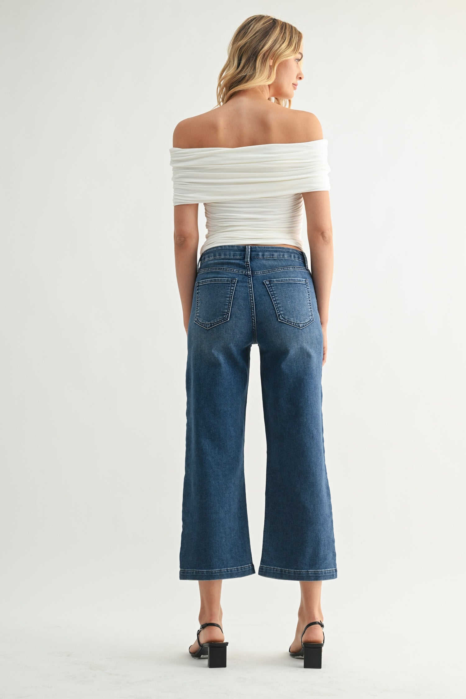 Woman wearing a white off-shoulder top and blue jeans on a plain background