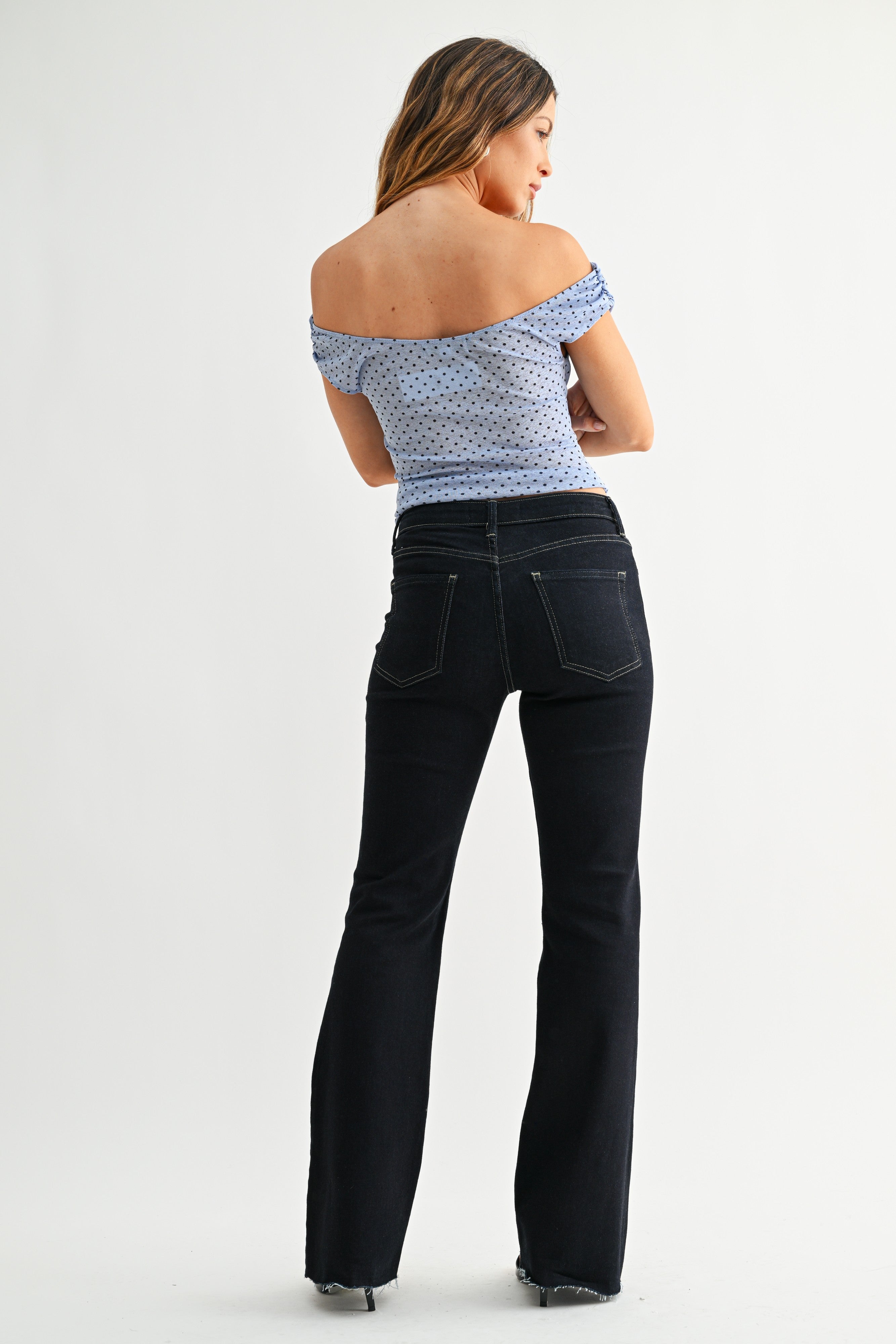 Back view of model wearing top with Super Dark Wash Flare Jeans against white studio background.