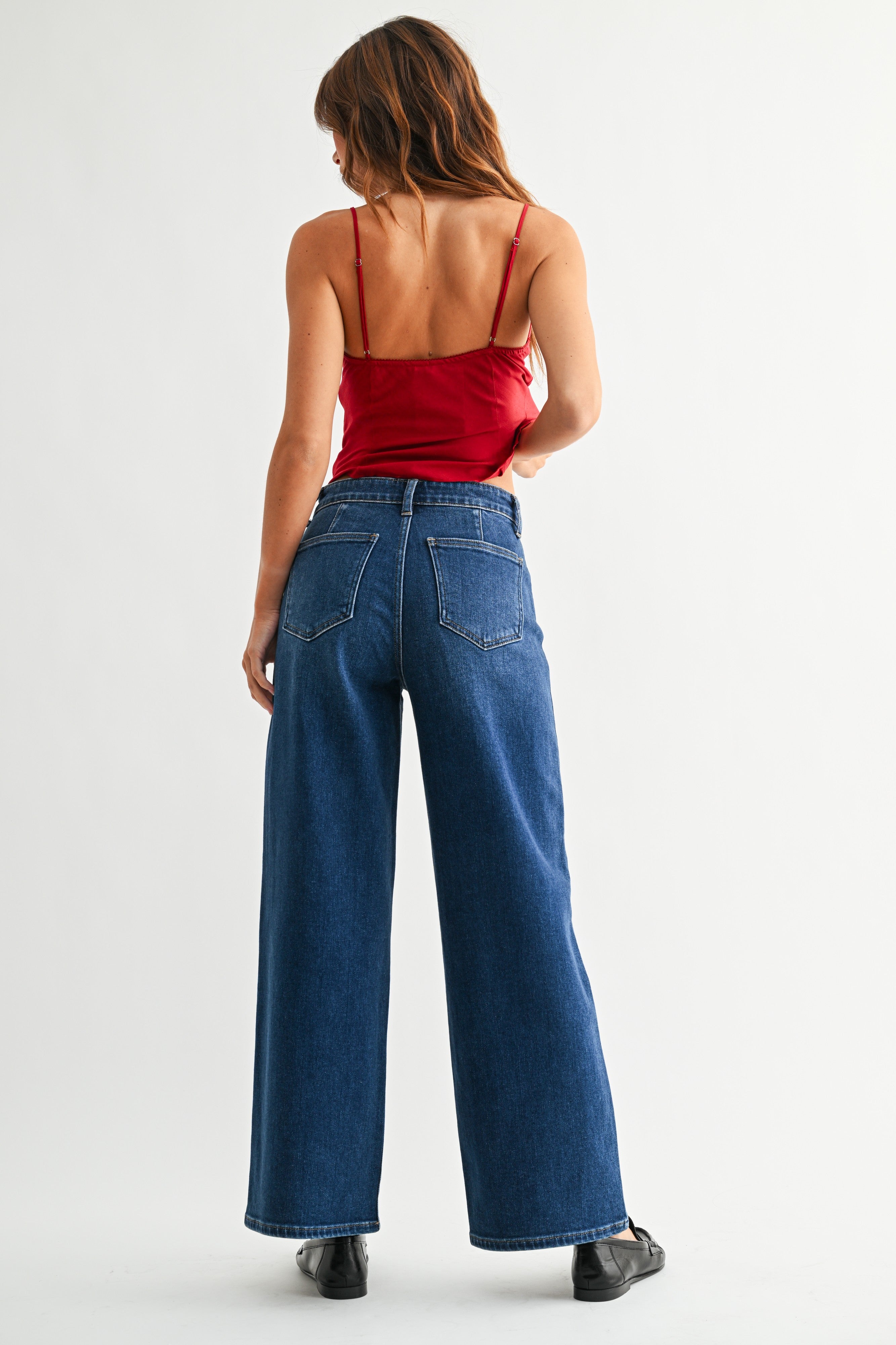 Back view of woman wearing red top with Dark Wash No Pocket Trouser Jeans against white studio background.