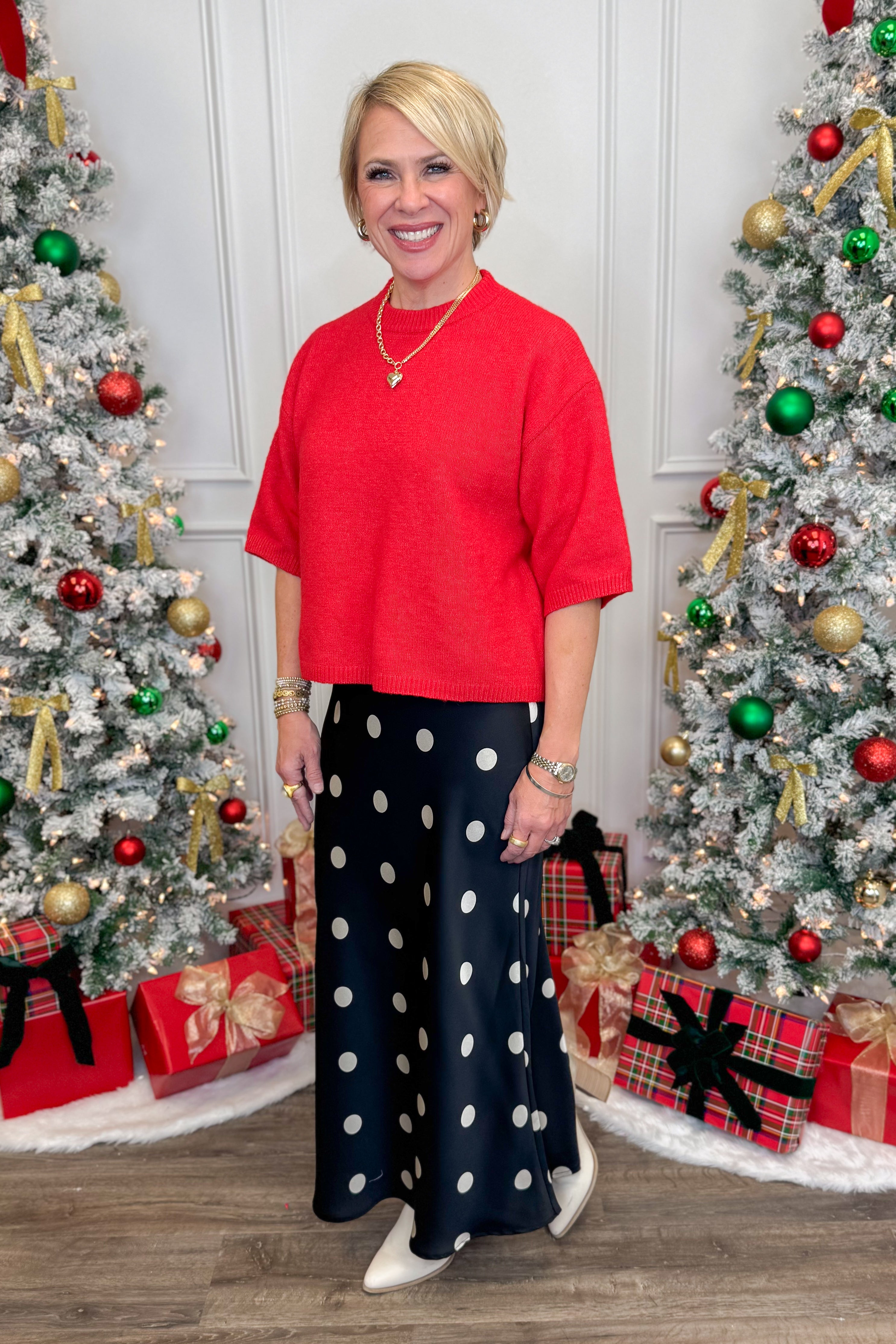 Woman in red top and polka dot pants standing between two decorated Christmas trees.