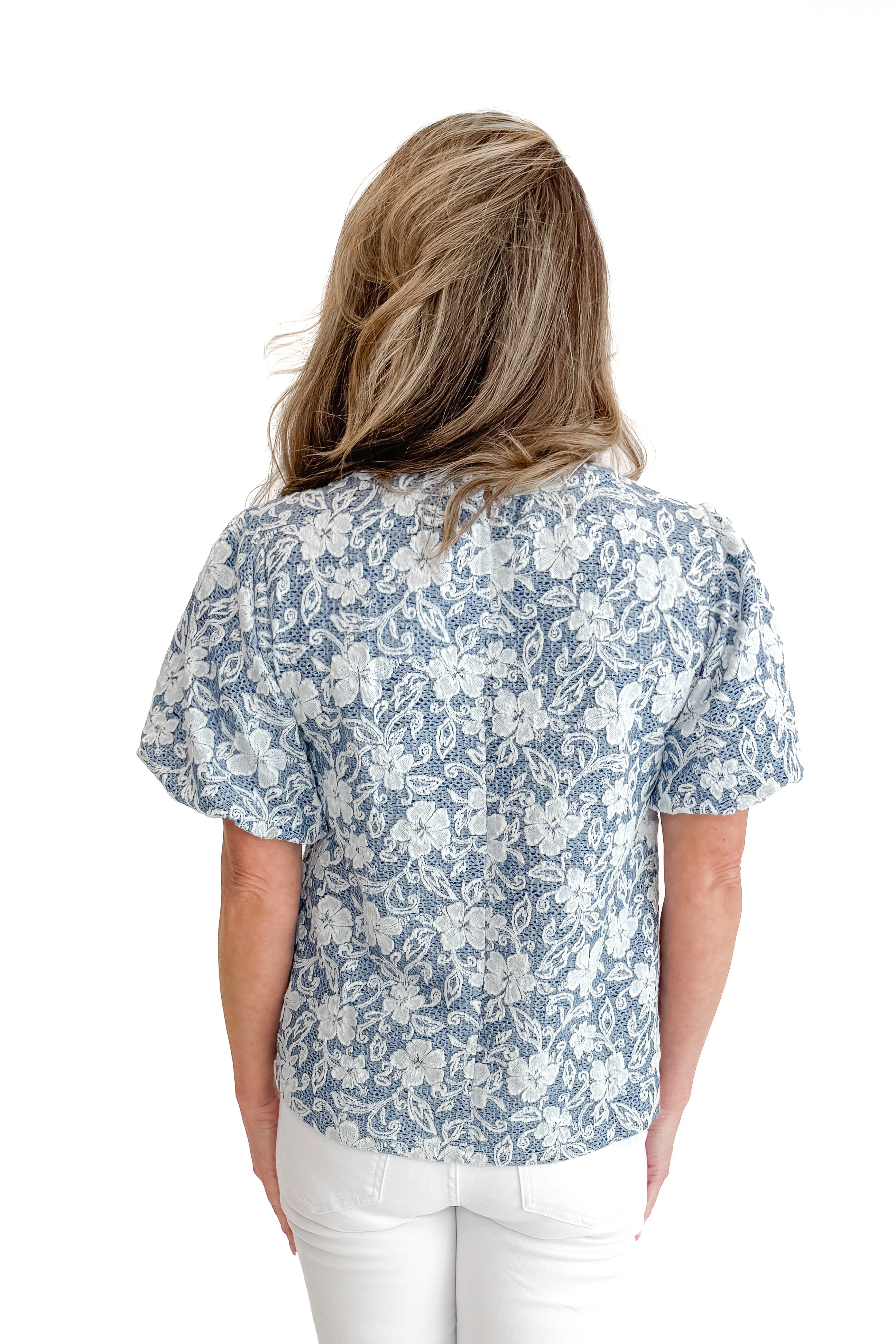 Back view of woman wearing Light Blue Floral Textured Top with jeans against white studio background.