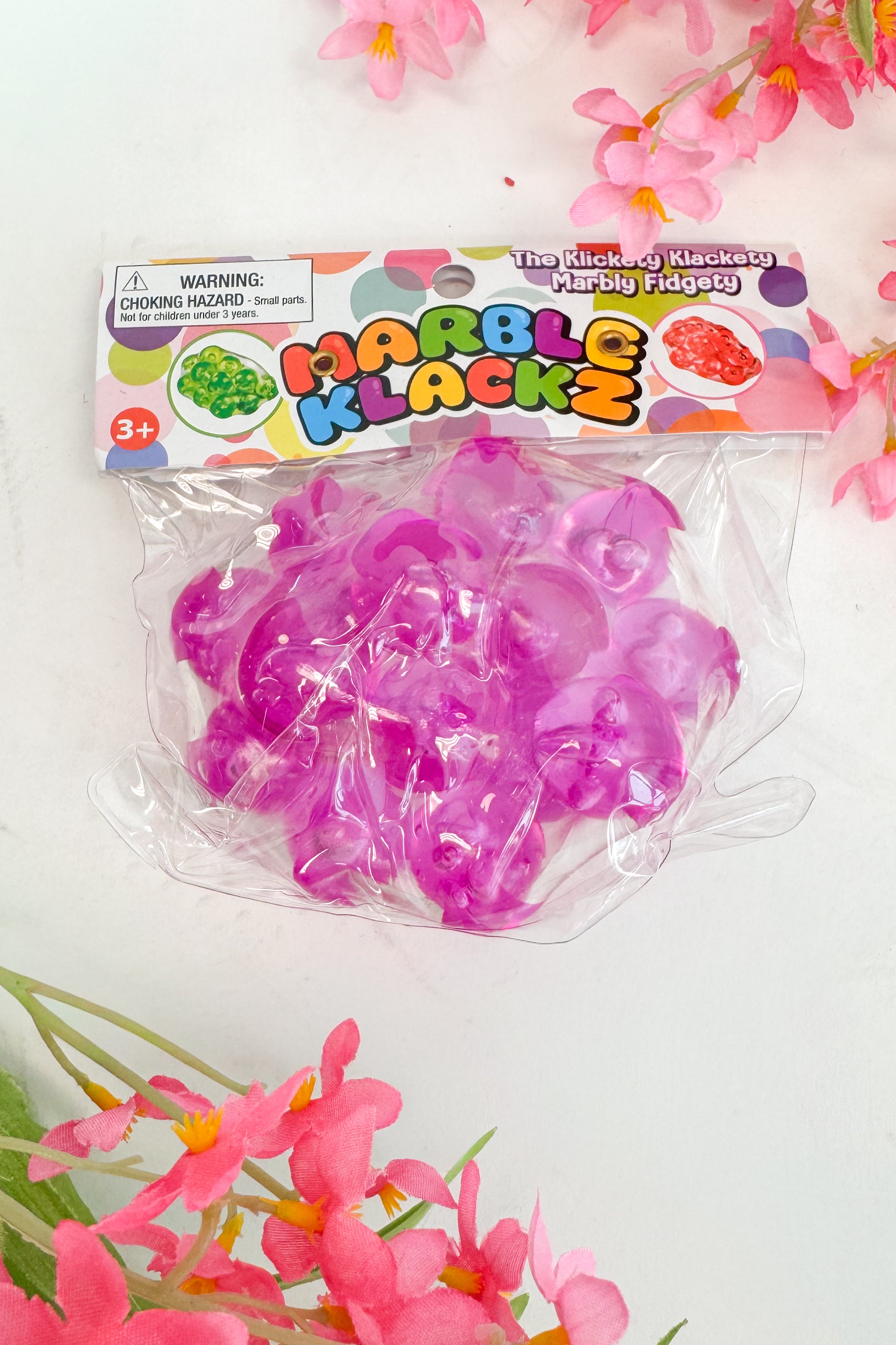 Marble Klackz toy packaging with pink toys and floral decorations on a light background