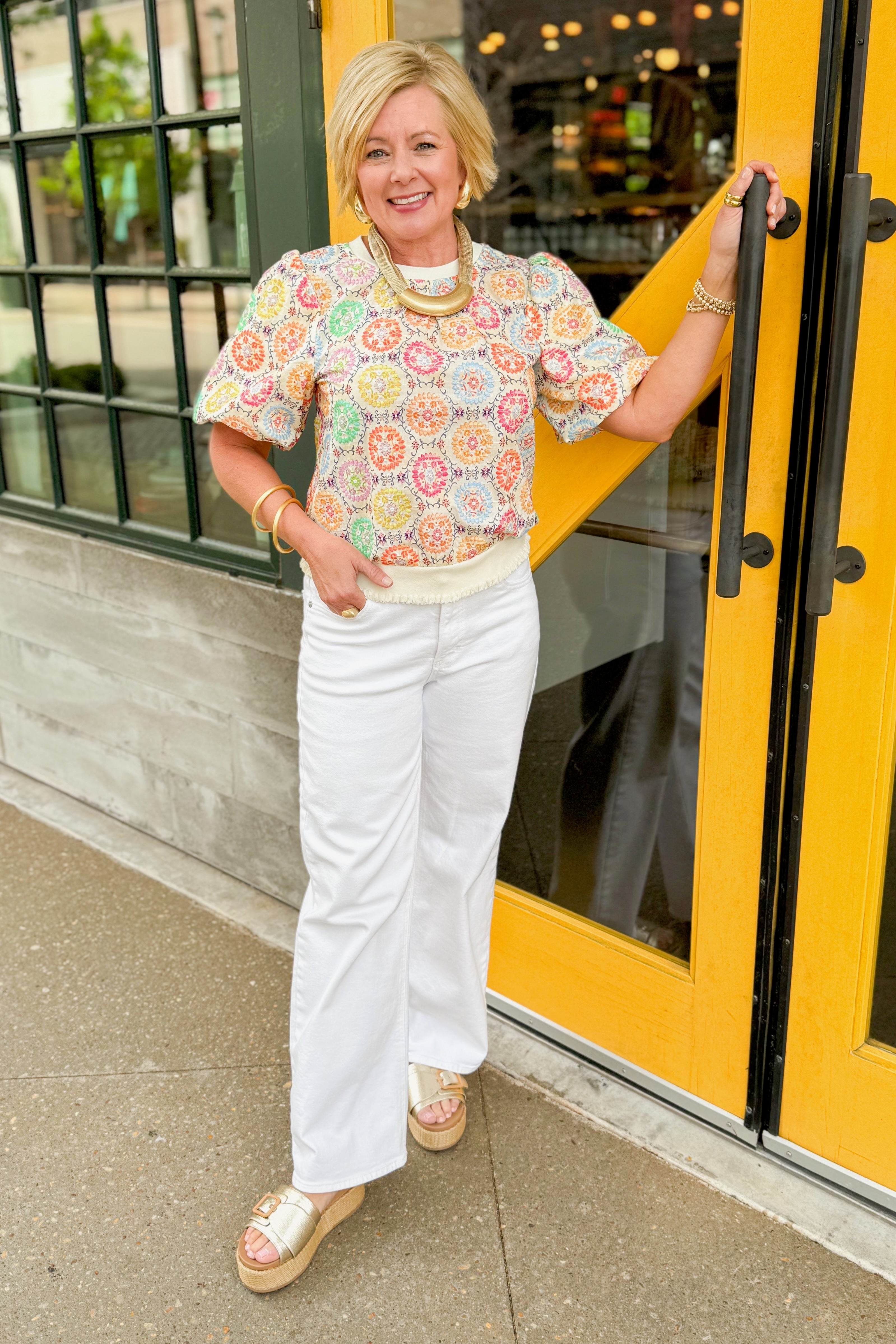 Front view of woman wearing Multi Circle & Floral Print Top with jeans and sandals outside at a restaurant.