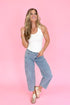 Woman wearing a white tank top and blue jeans against a pink background