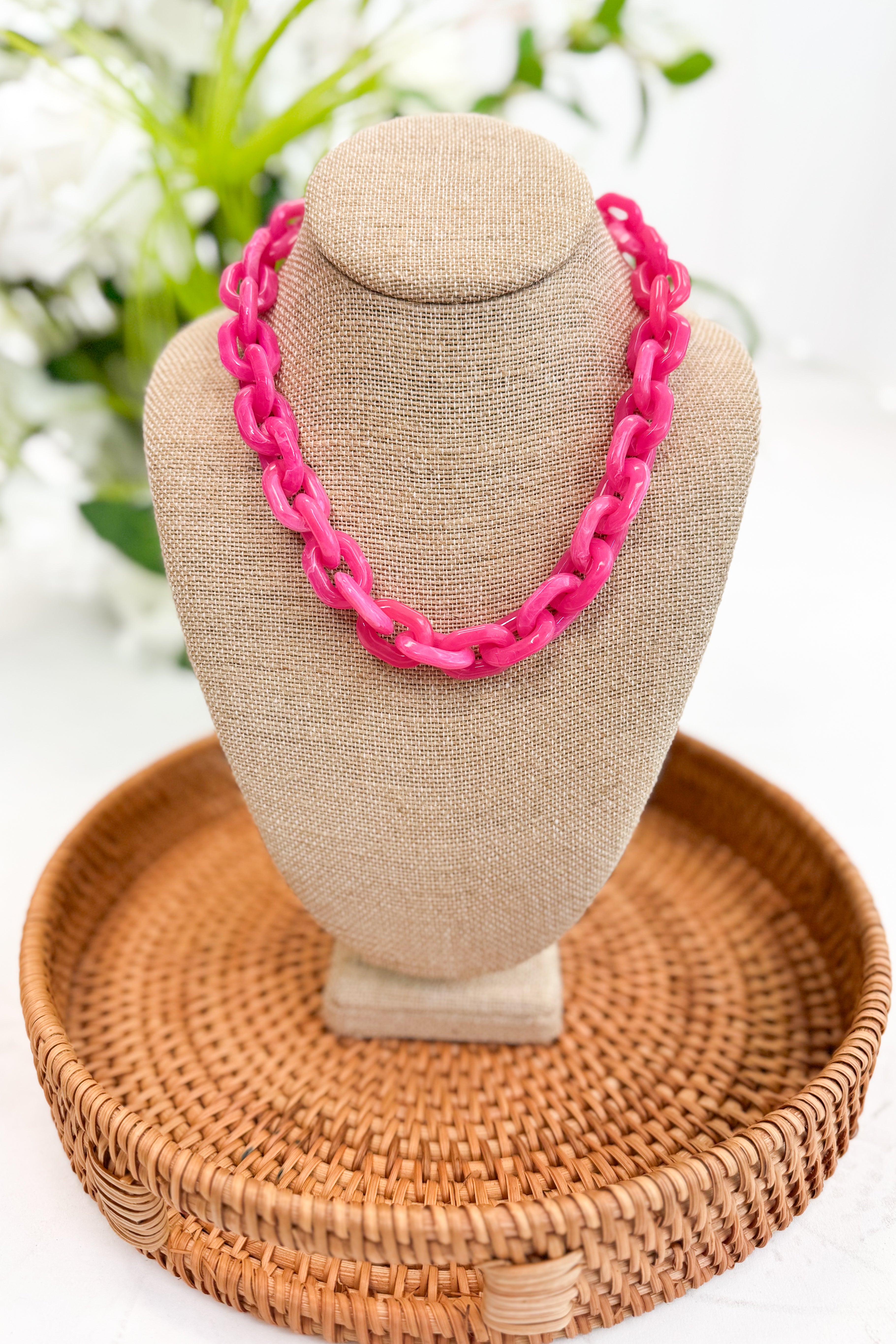 Necklace on a beige mannequin bust with a woven basket and blurred greenery in the background