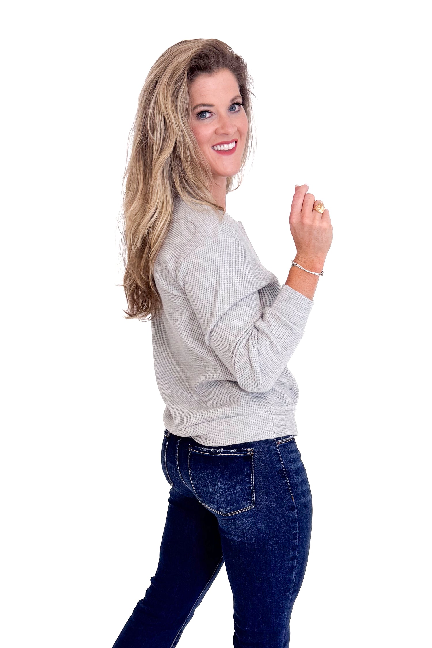 Woman wearing a gray sweater and dark jeans on a white background