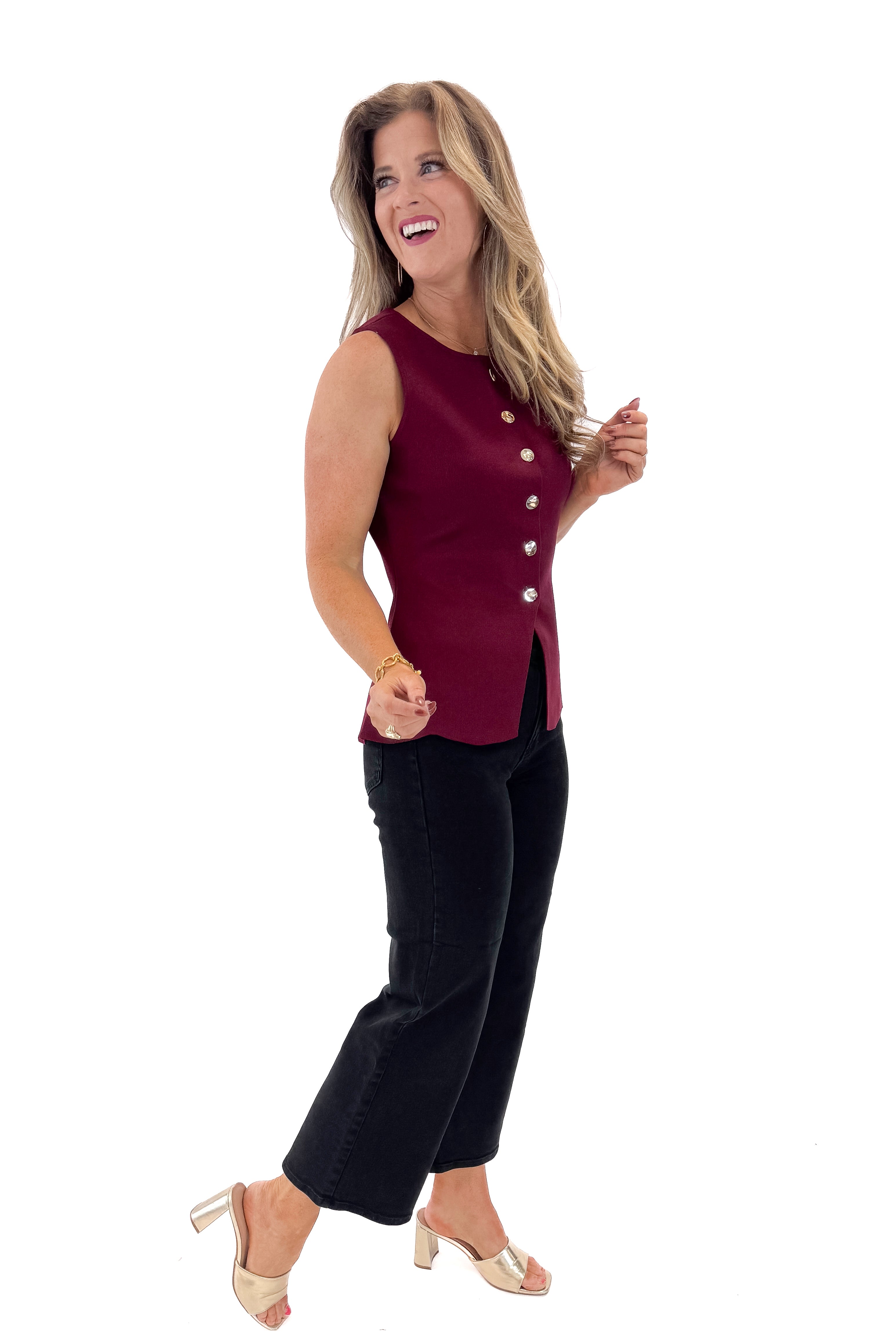 Side view of woman wearing Burgundy Button Detail Sleeveless Peplum Sweater with jeans against white studio background.
