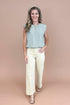 Woman wearing a light blue sleeveless top and cream pants on a beige background