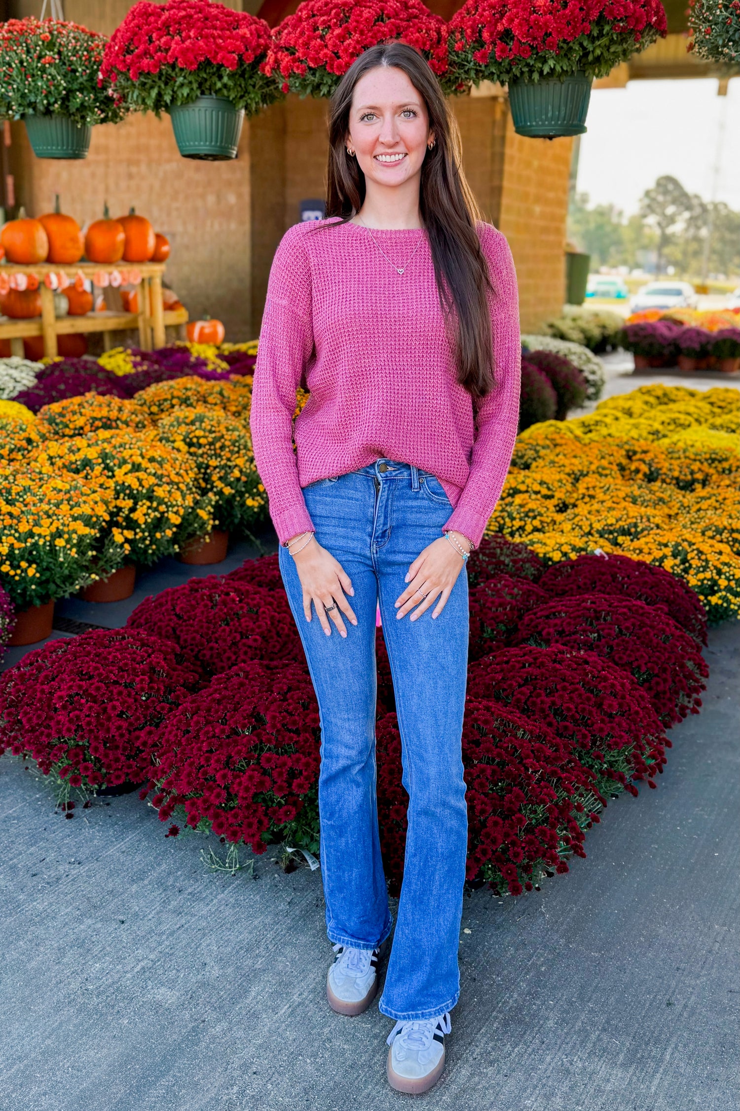Outdoor picture of woman wearing Rose Waffle Knit Sweater and jeans with mums in the background.