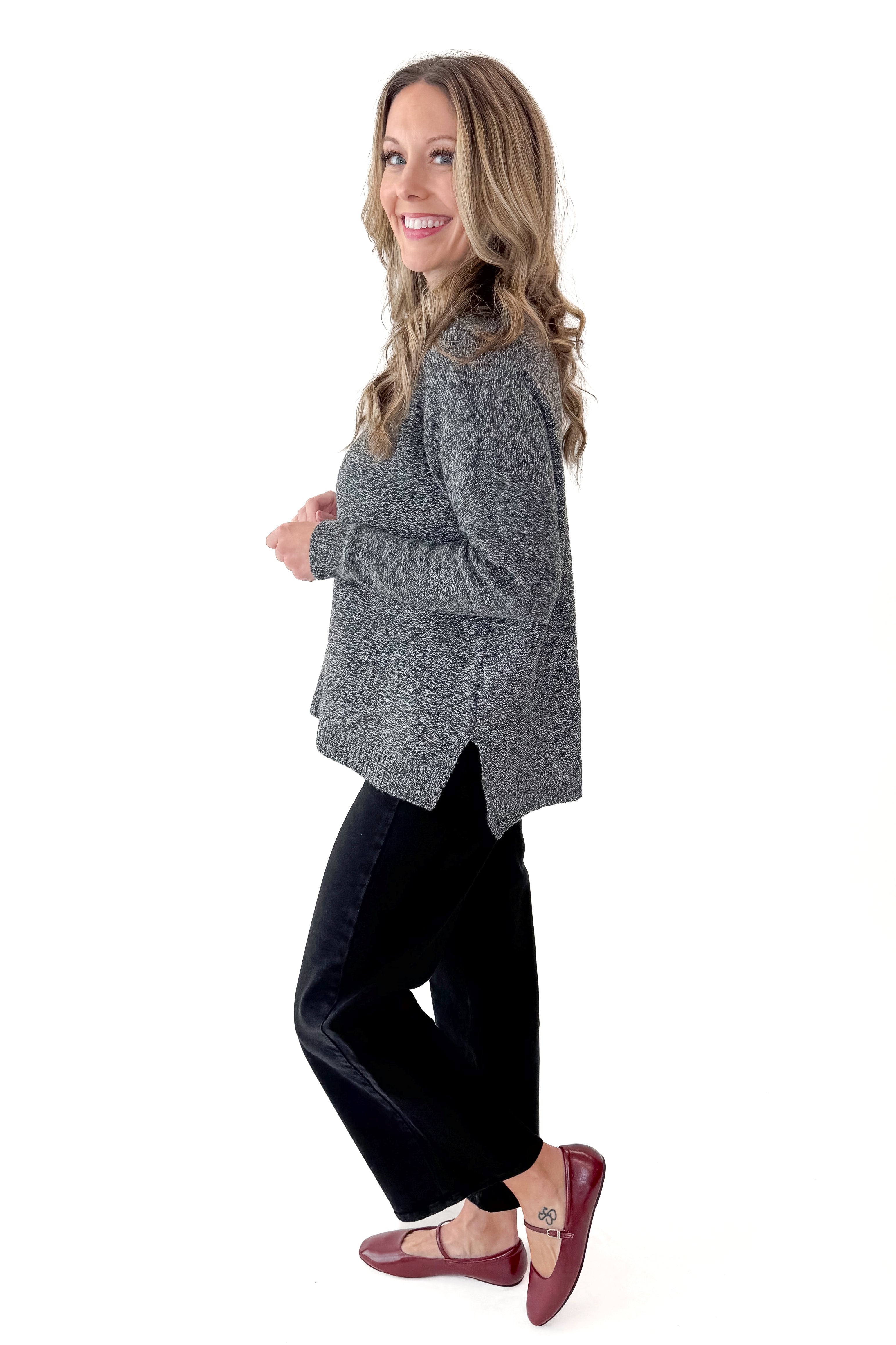 Side view of woman wearing Black & Cream Marled Mock Neck Sweater with jeans against white studio background.