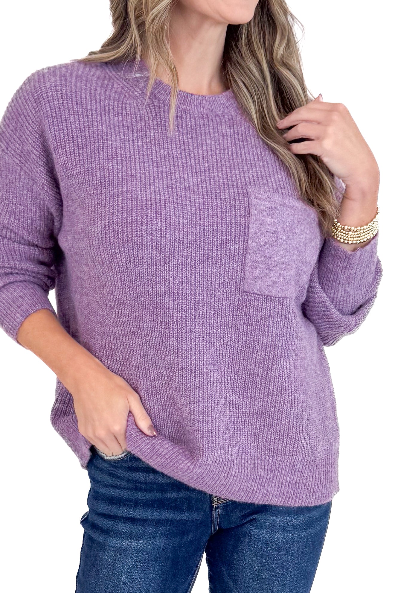 Woman wearing a purple sweater with a pocket, standing against a plain background.