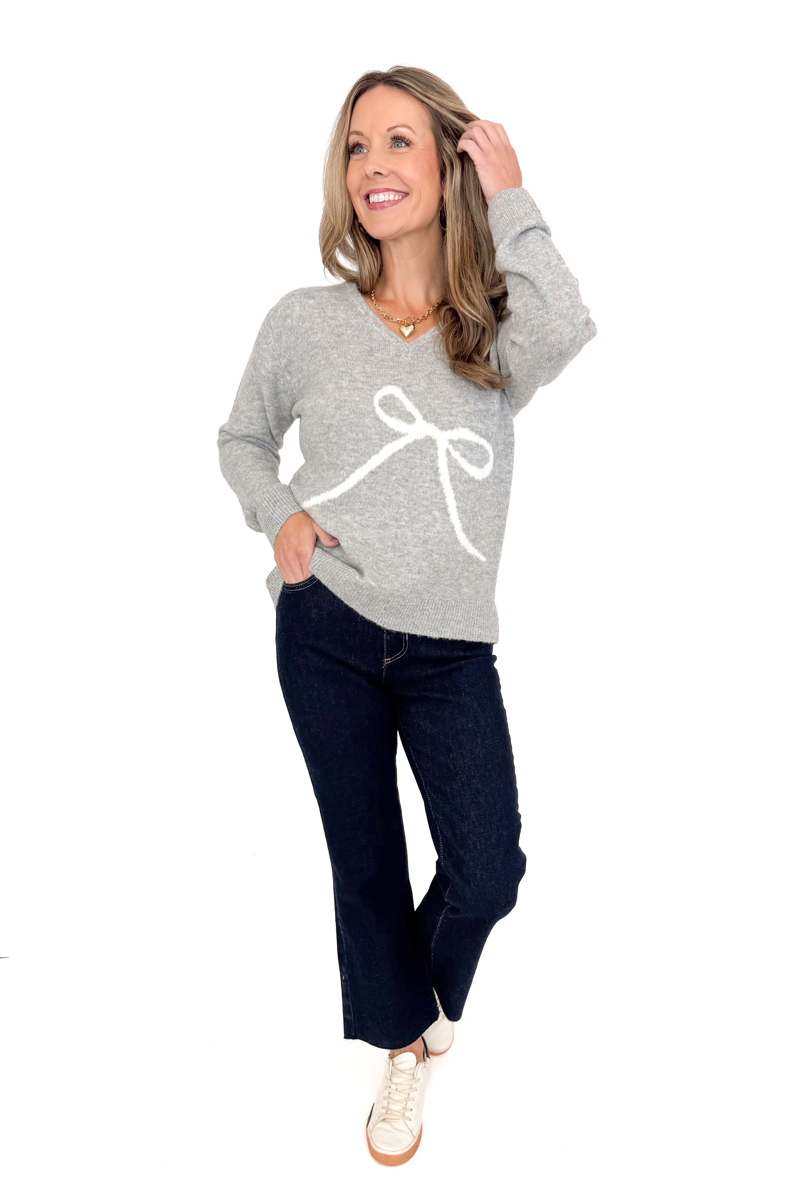 Front view of woman wearing Grey Bow Printed Sweater with jeans against white studio background.