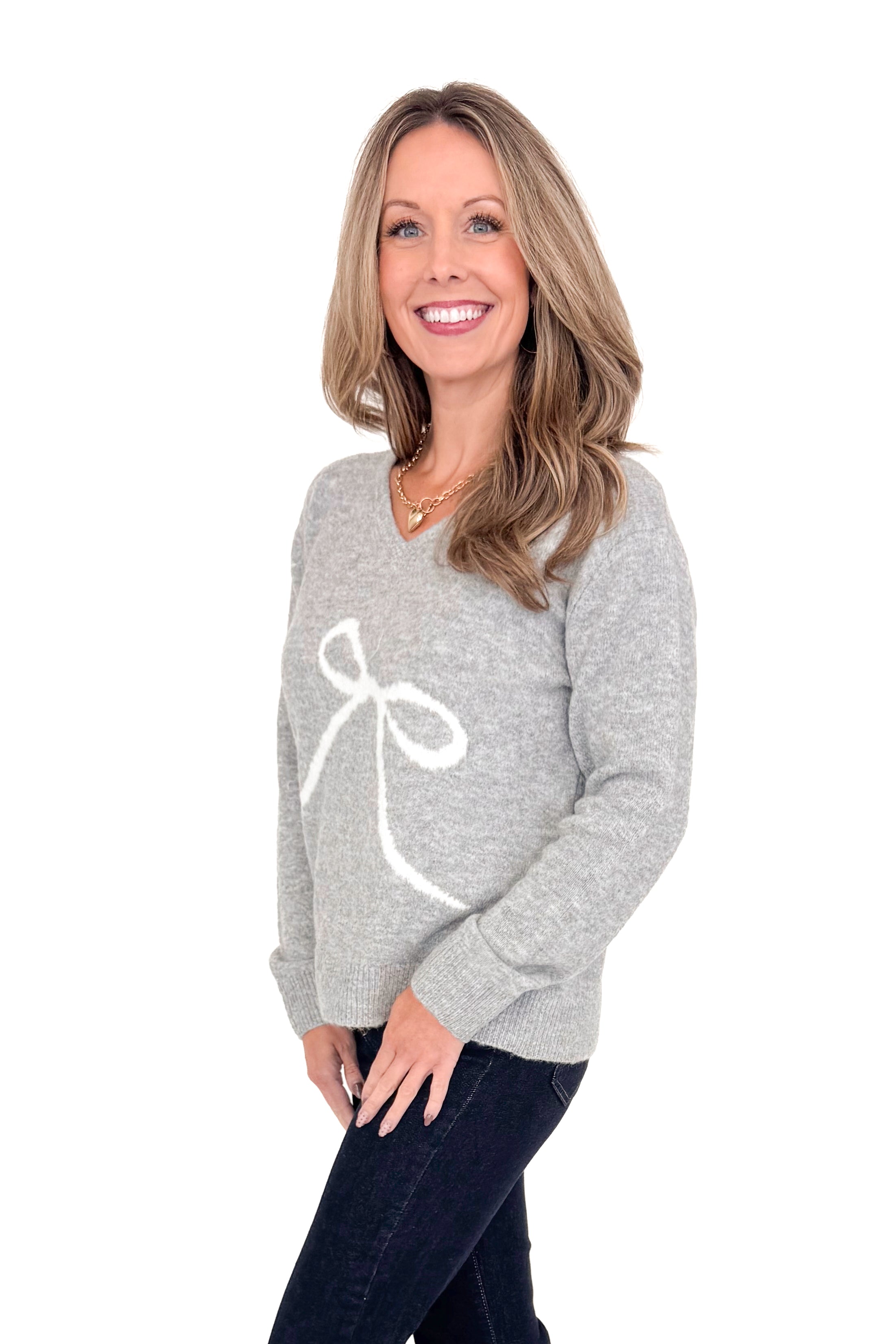 Side view of woman wearing Grey Bow Printed Sweater with jeans against white studio background.