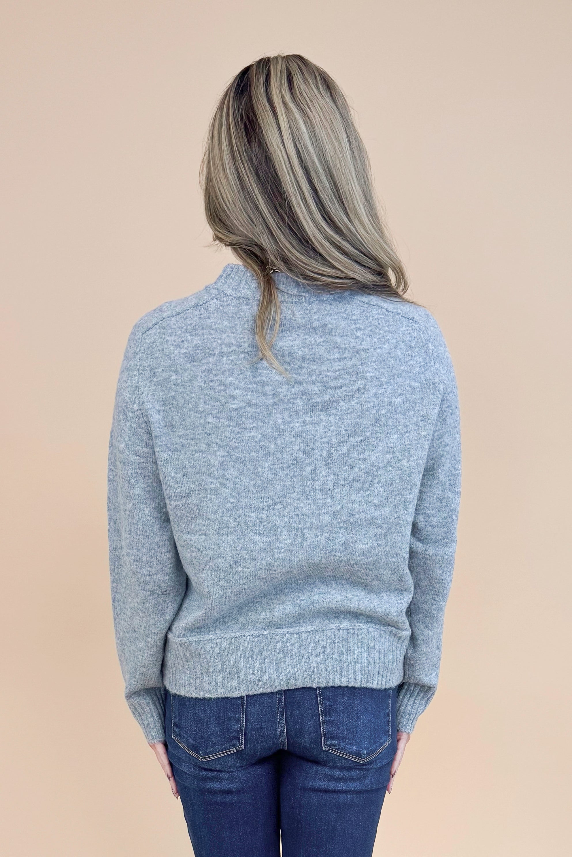 Back view of woman wearing Grey Center Seam Detail Sweater and blue jeans.