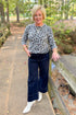 Front view of woman outside wearing Grey Leopard Crewneck Sweater with jeans against with leaves and trees in the background.