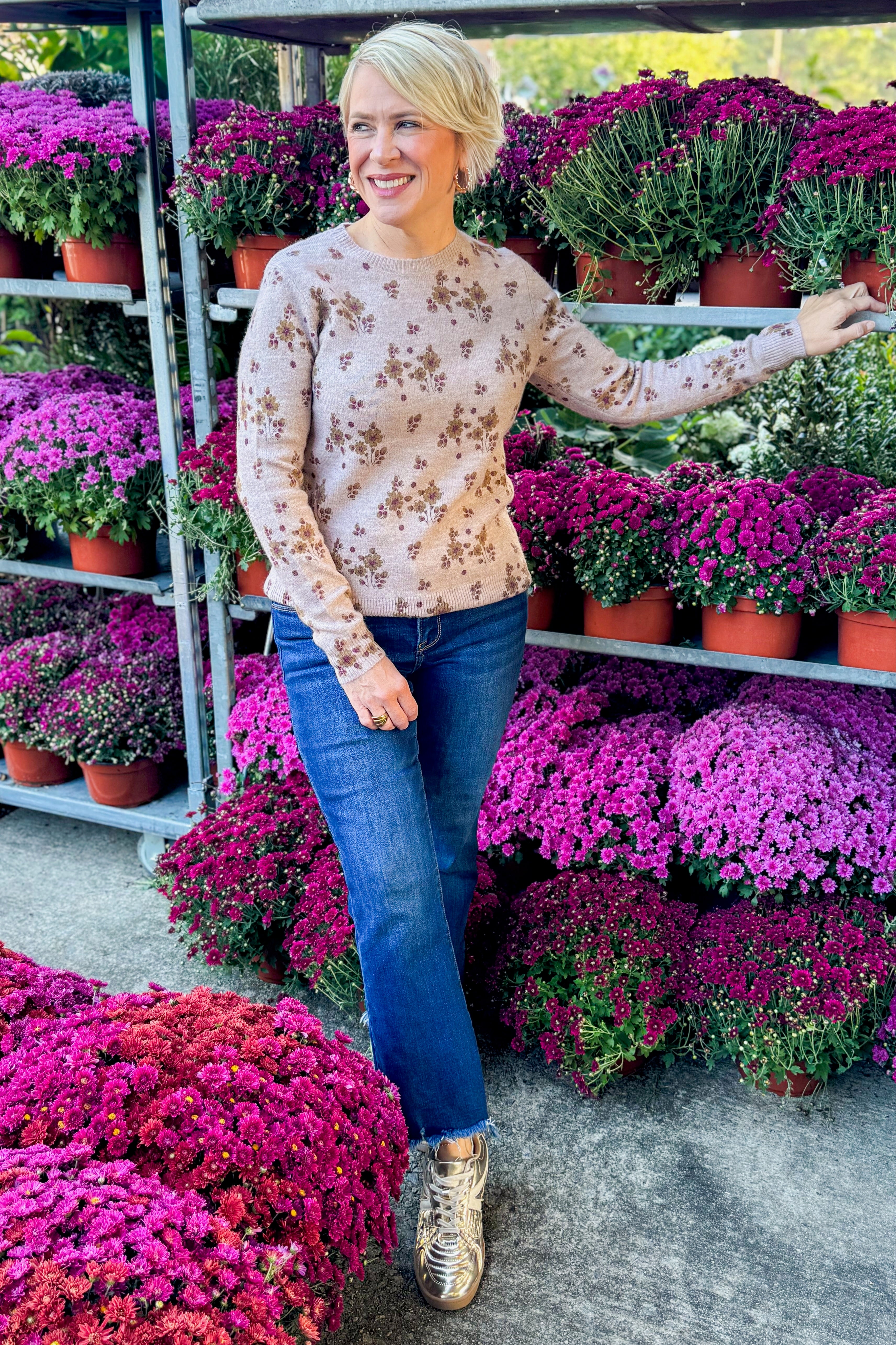 Woman wearing Blush Floral Print Sweater and jeans outside by purple mums.