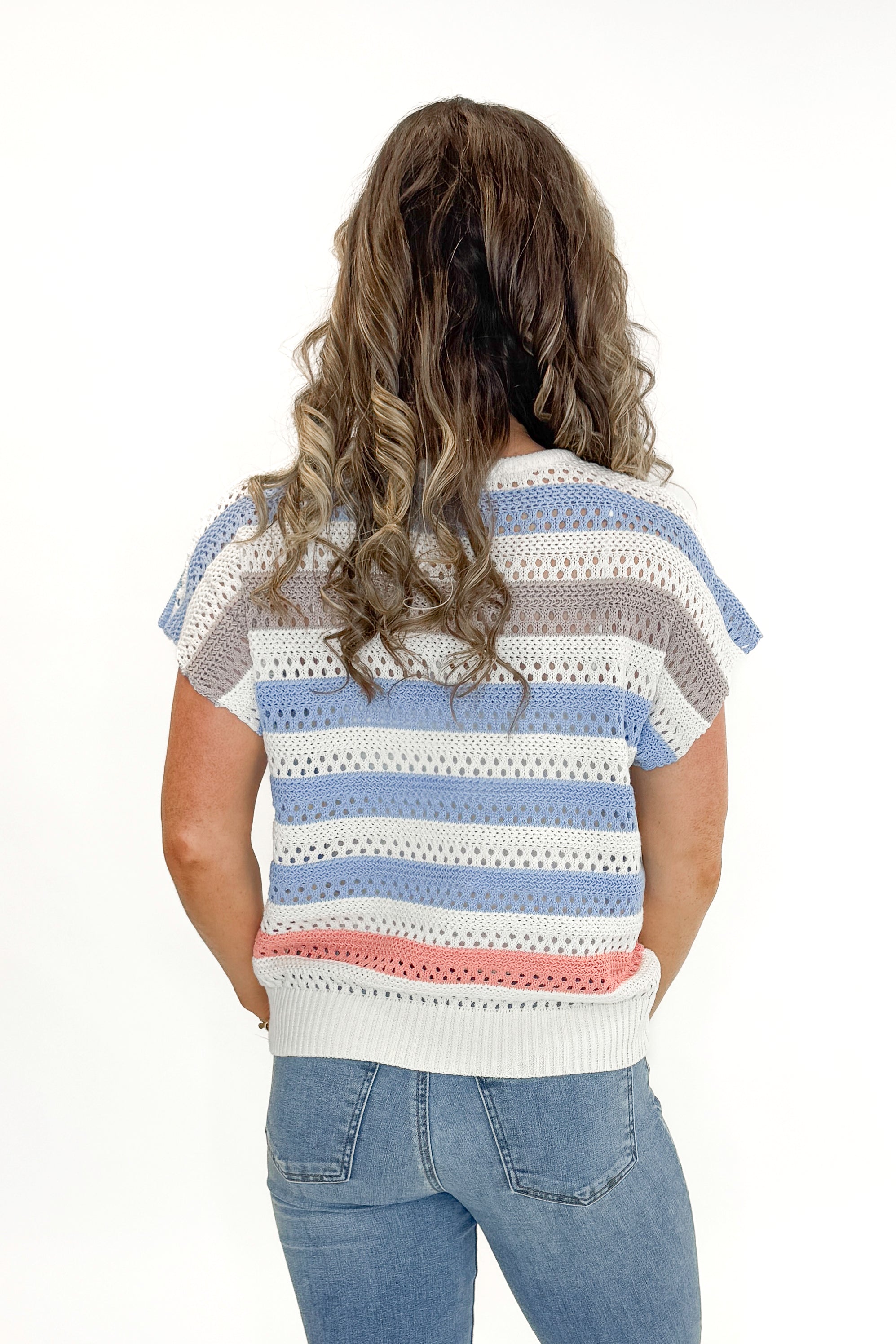 Back view of woman wearing Cream & Multi Striped Crochet Sleeveless Sweater with jeans against white studio background.