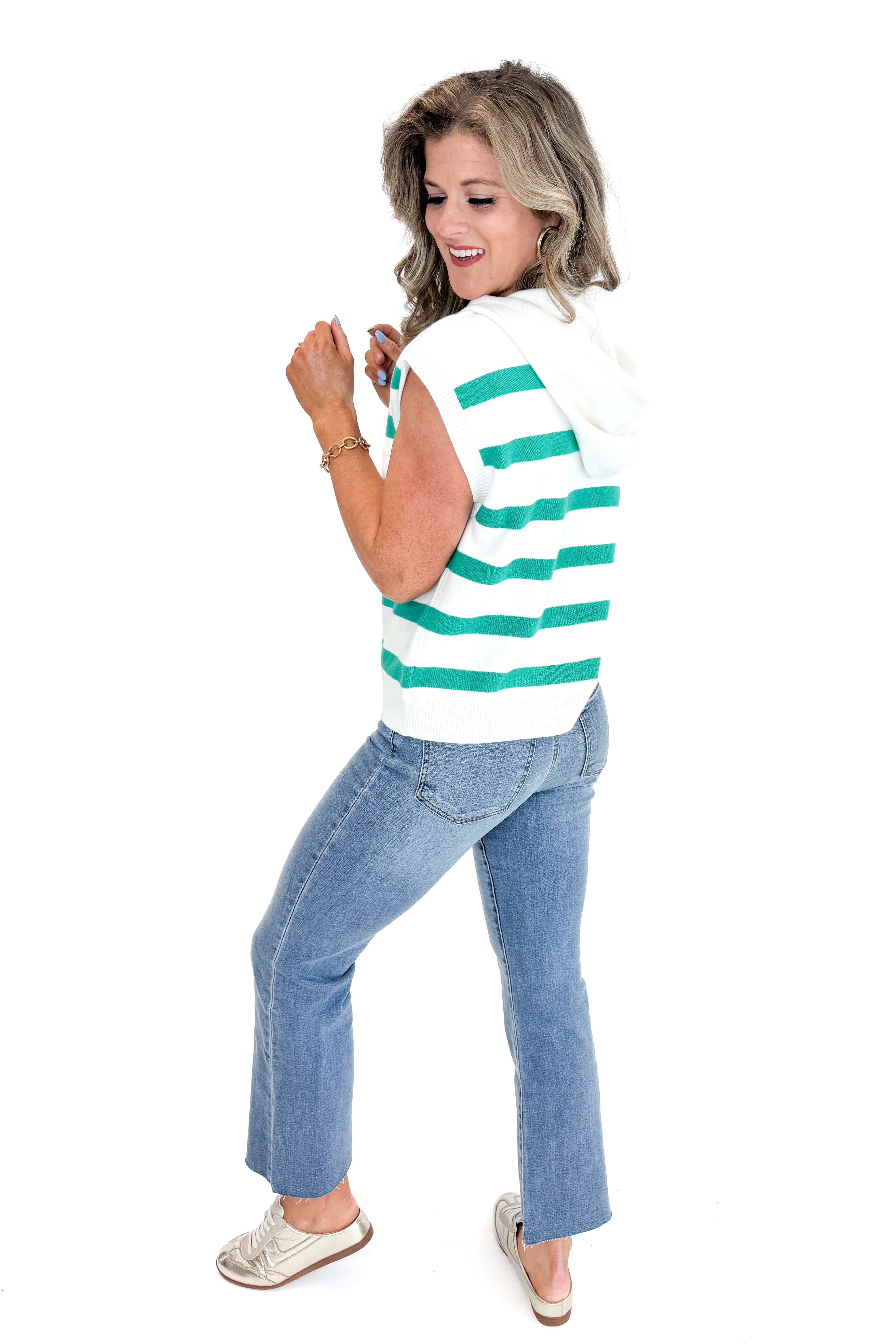 Side view of woman wearing Green Striped Sleeveless Sweater with jeans against white studio background.