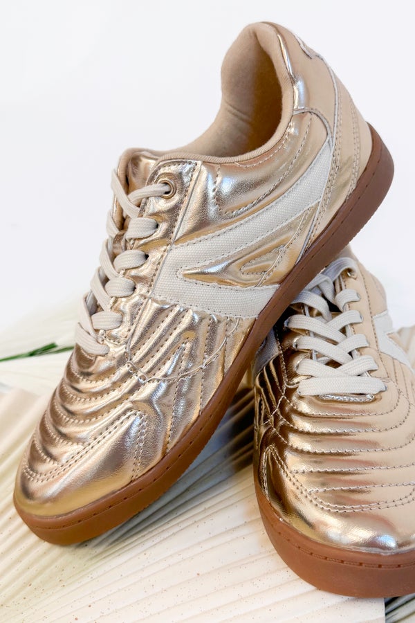 Pair of gold sneakers with brown soles on a light wooden surface