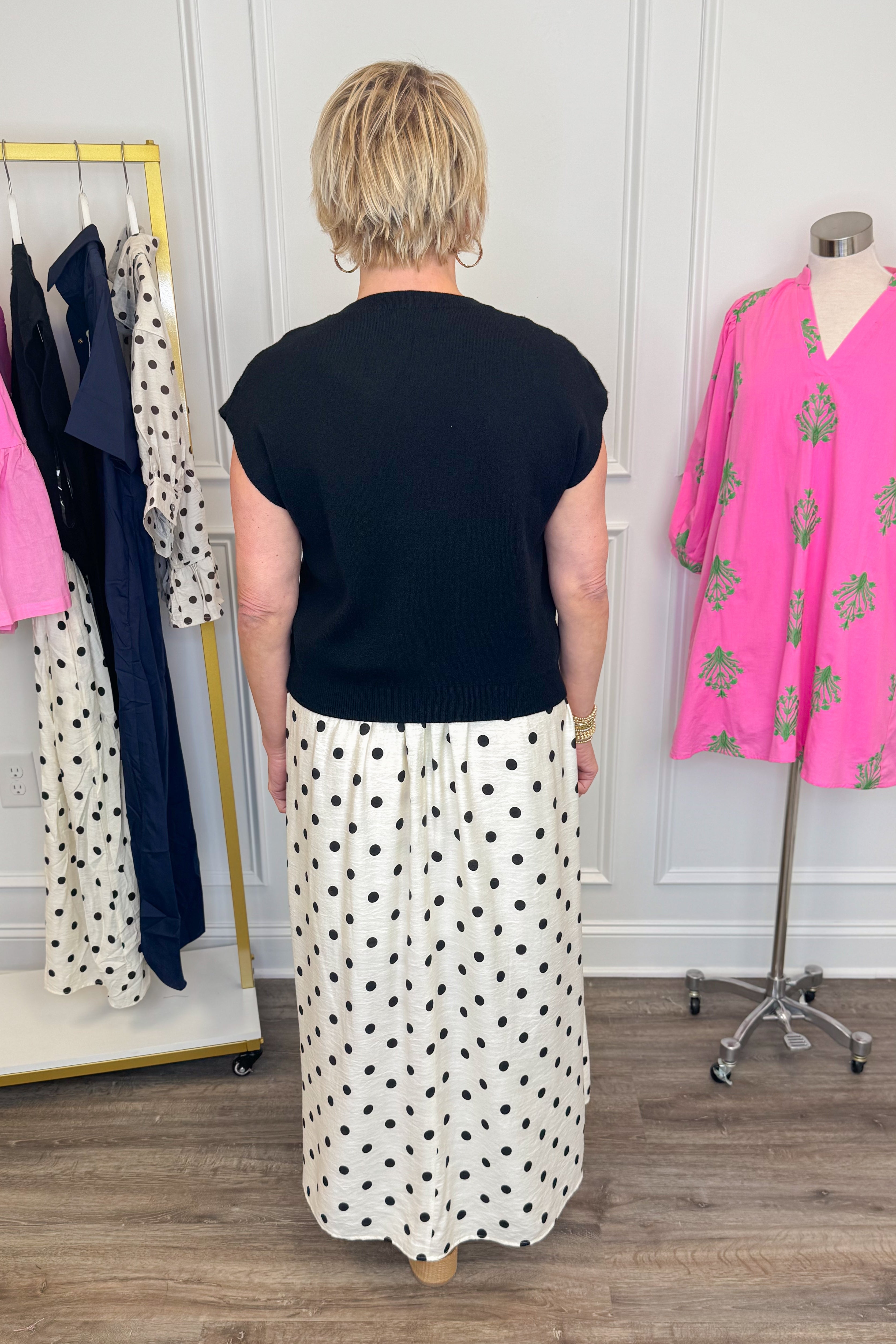 Back view of woman wearing Swagger Boutiqueβs Black & Cream Polka Dot Layered Midi Dress by Entro with sandals at the store.