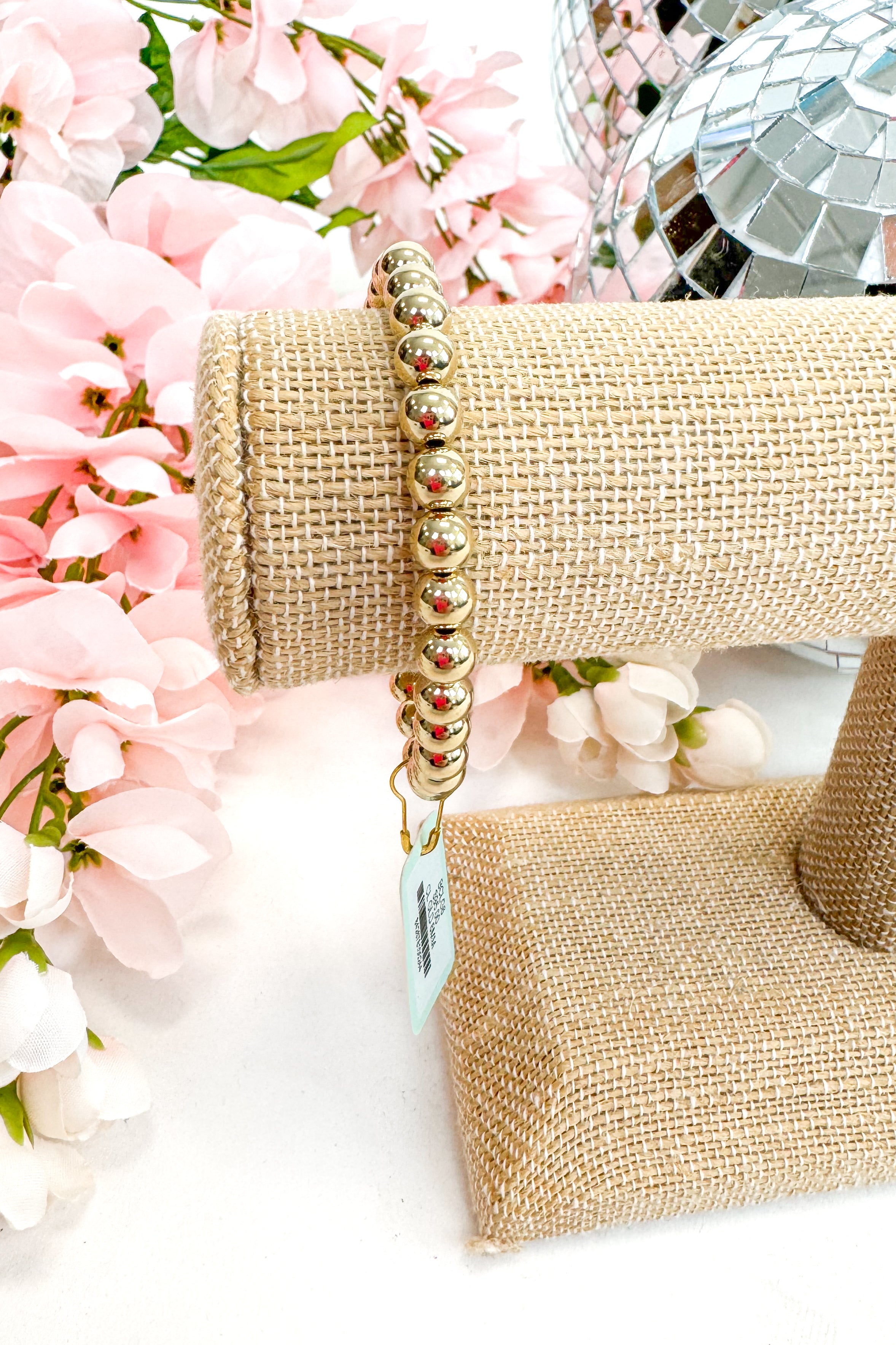 gold enewton bracelet on burlap display with floral background