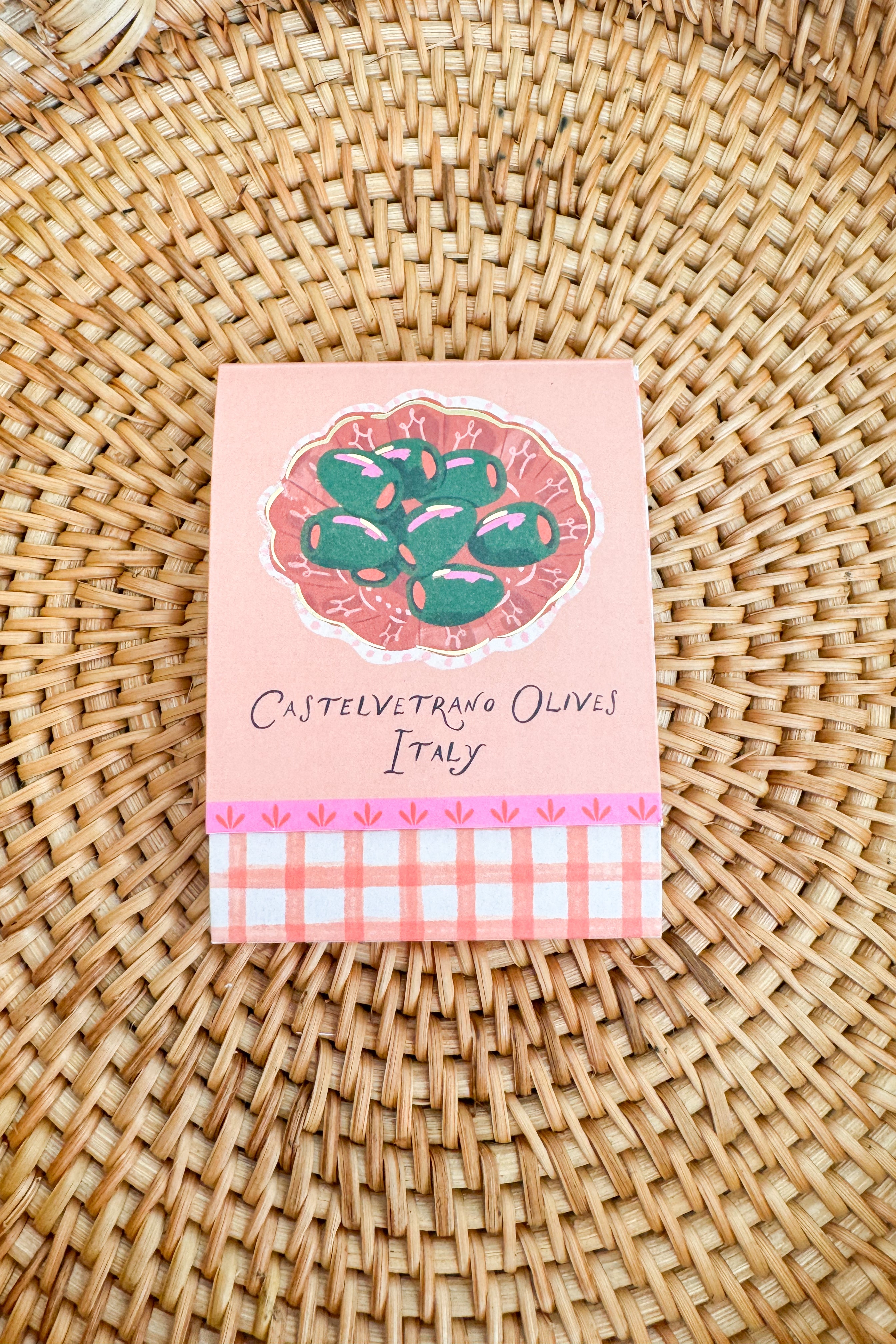 Small pink packaging with olive design on a woven surface