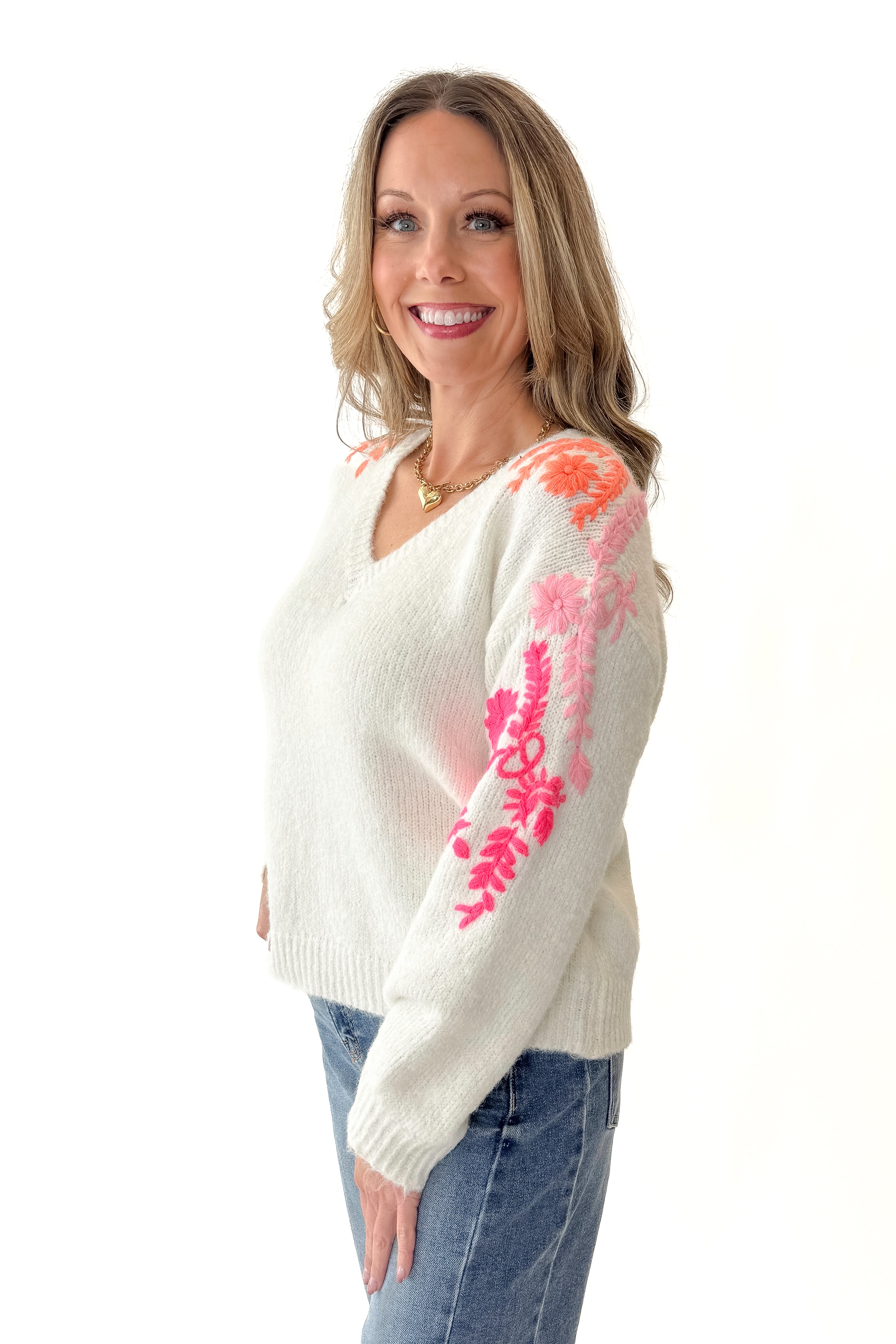 Side view of woman wearing Ivory With Floral Embroidery Sweater with jeans against white studio background.