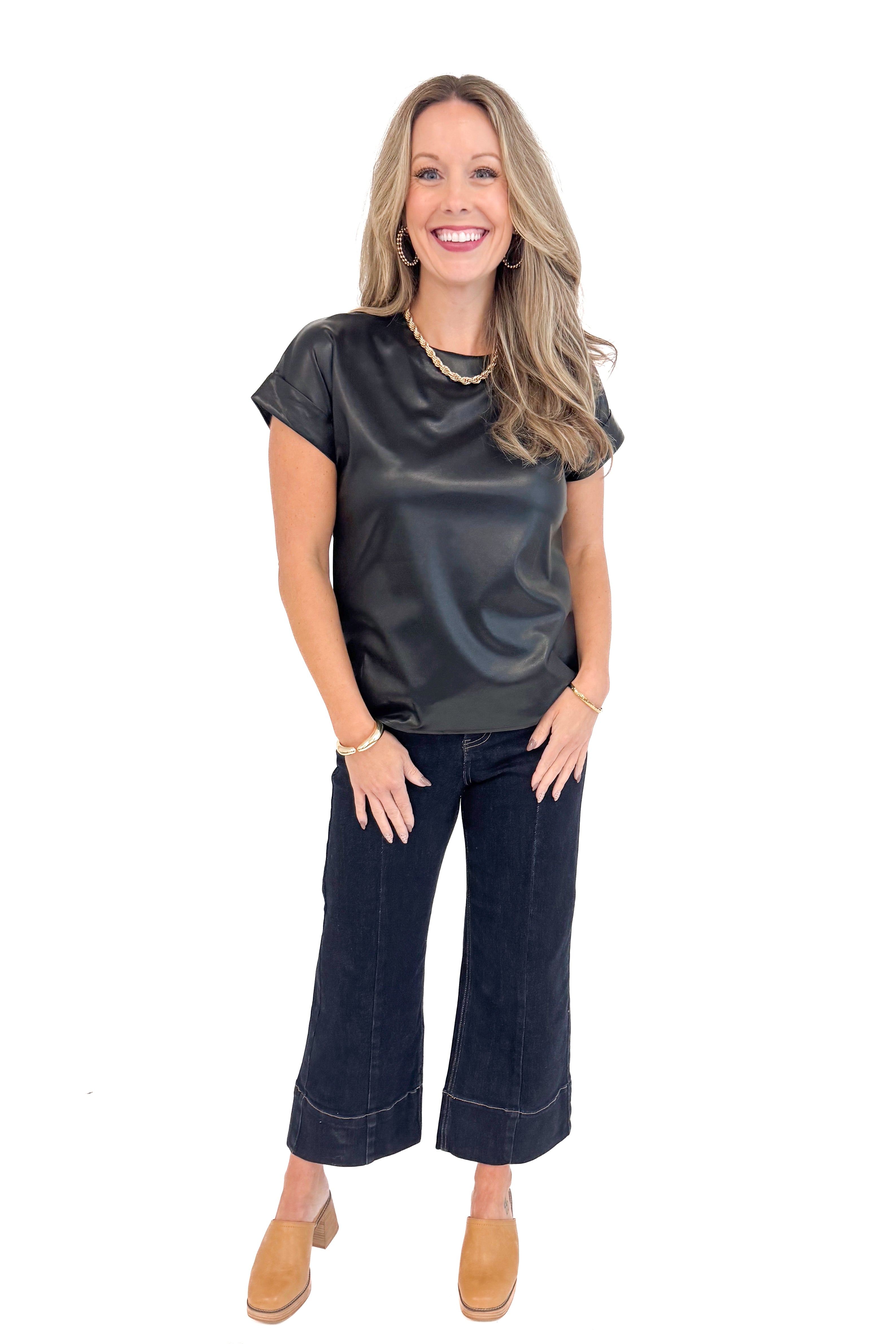 Full length woman wearing black faux leather cap sleeve top with round neckline and blue jeans.