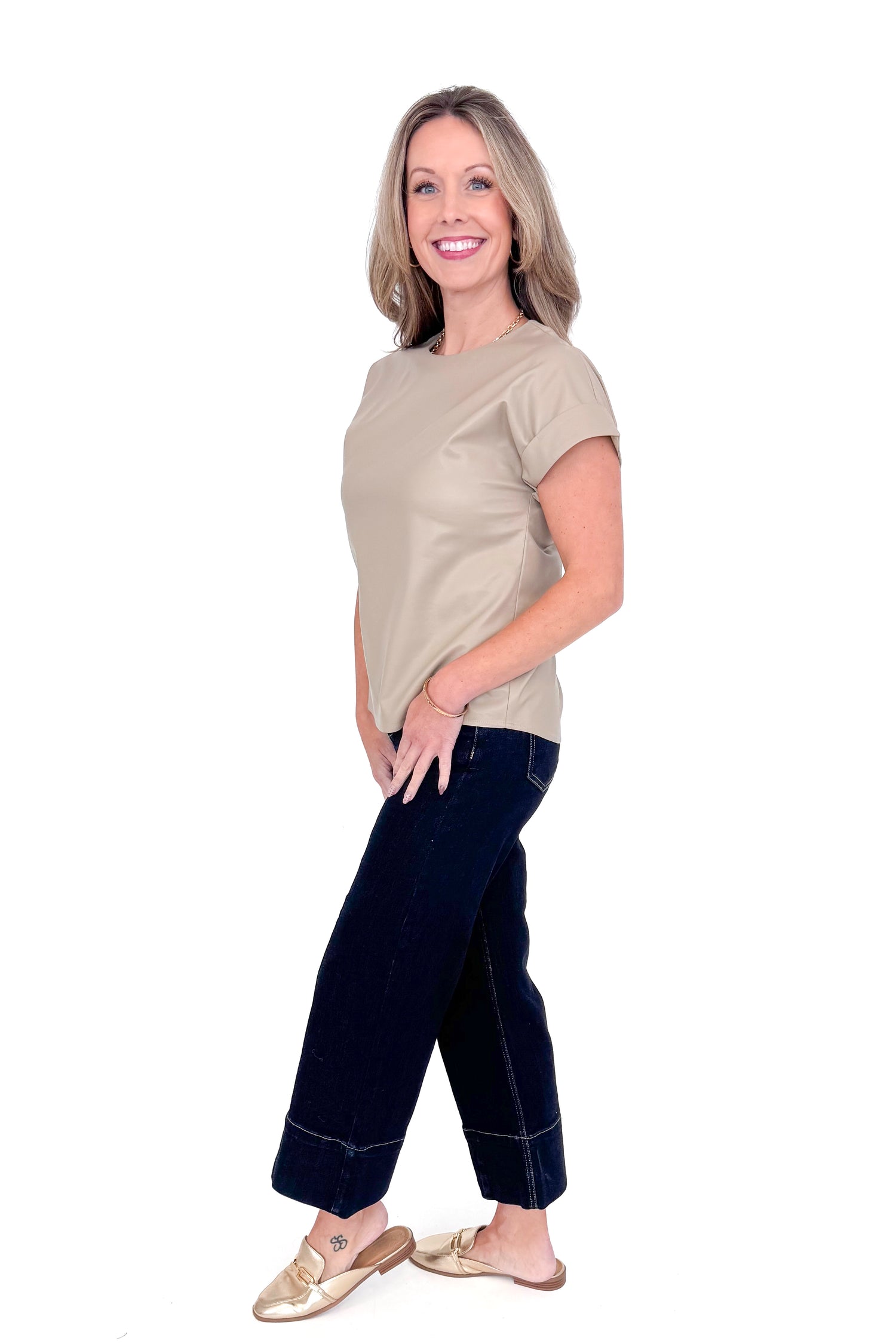 Side view of woman wearing taupe faux leather top with jeans against white studio background.