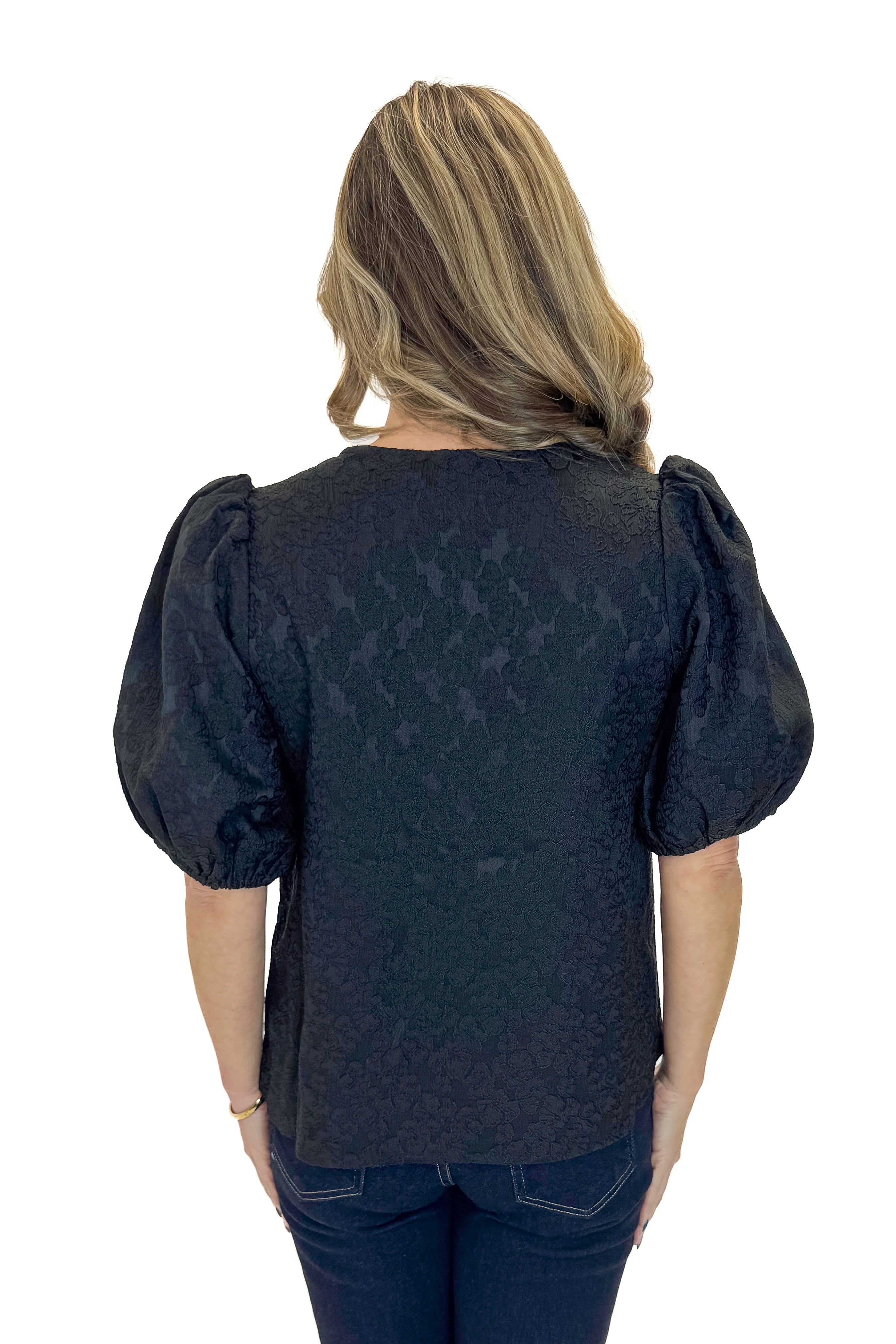 Back view of woman wearing Black Lace Ren Top with jeans against white studio background.
