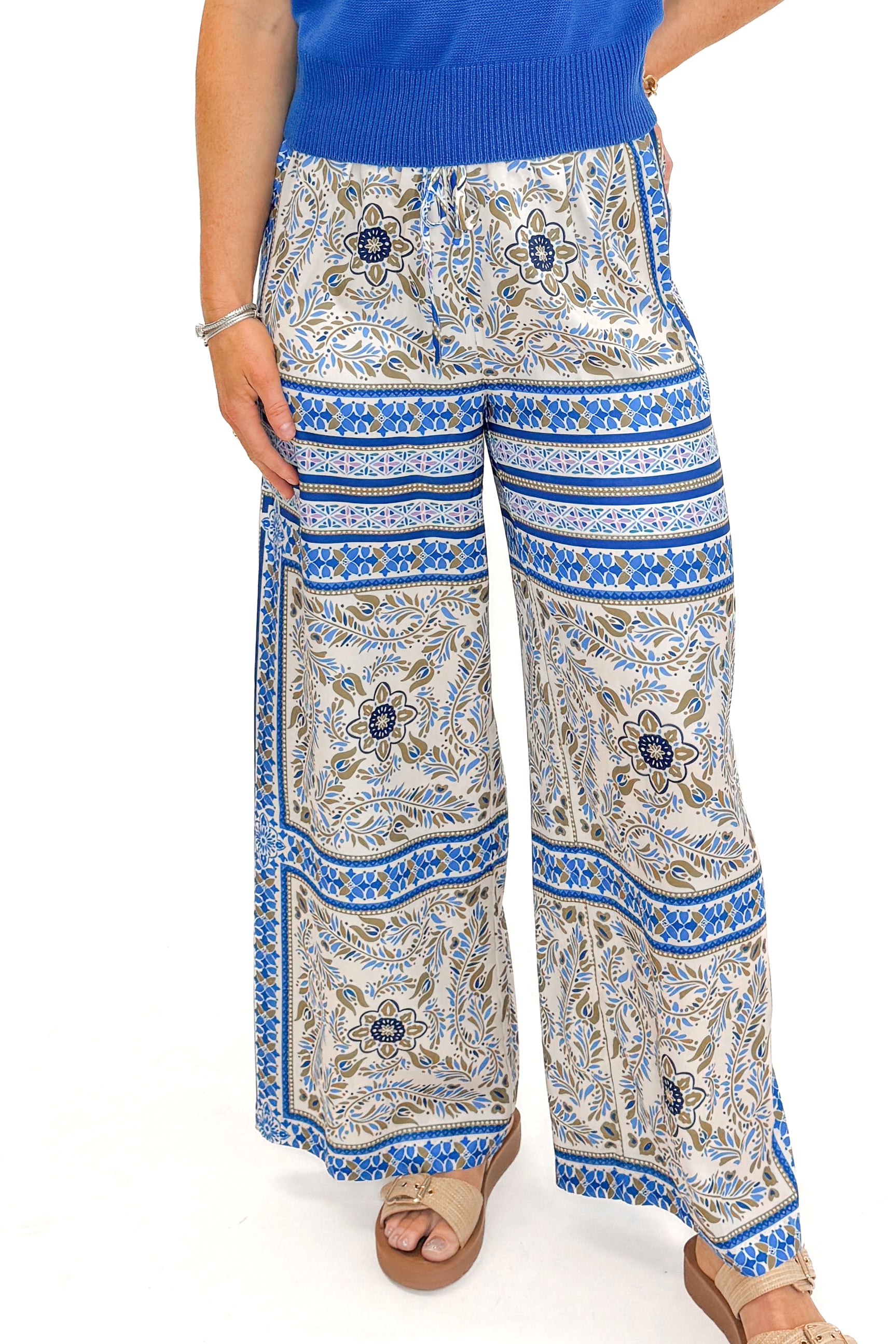 Front detail view of woman wearing Blue & Multi Scarf Print Pants by PINCH with blue sweater against white studio background.
