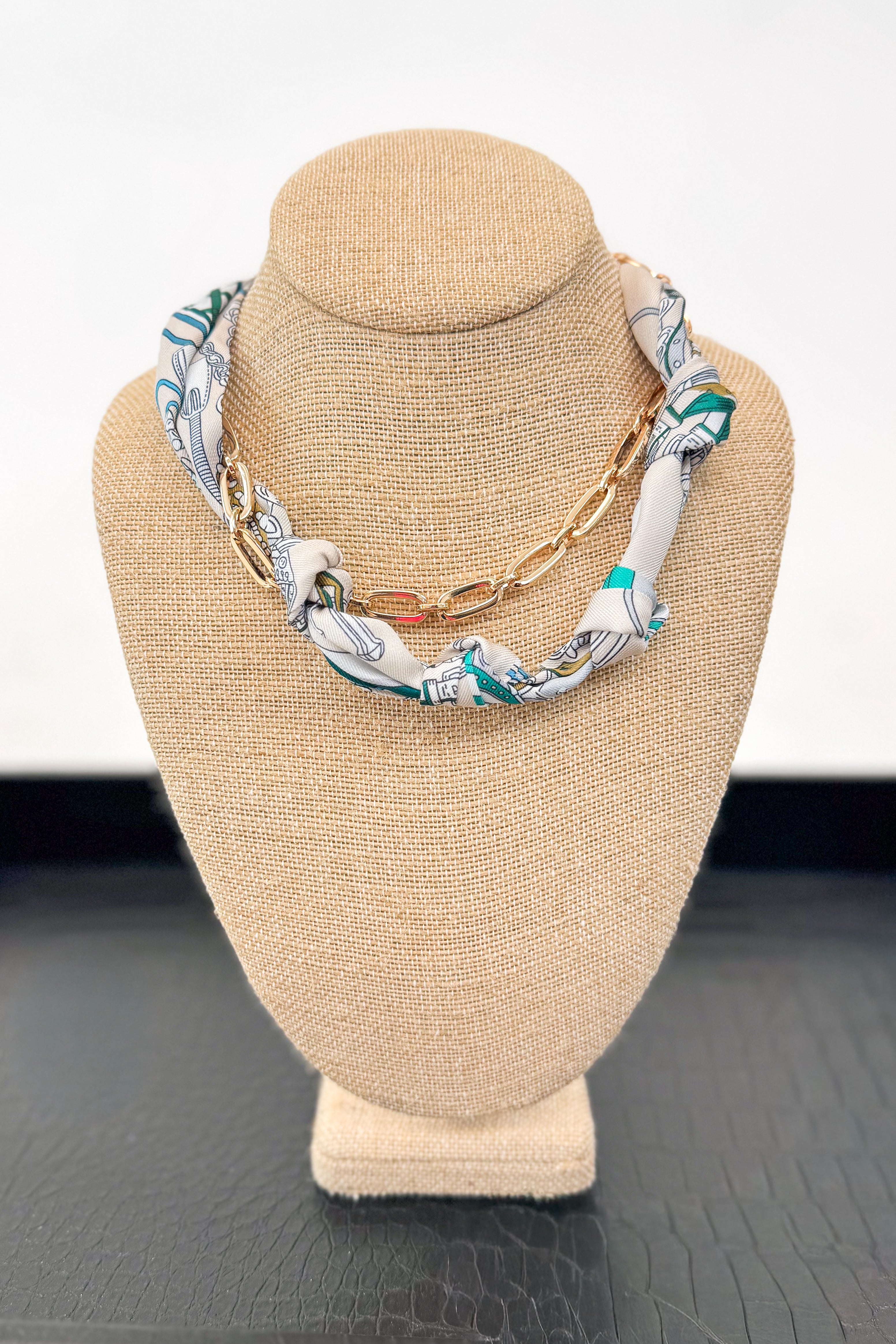 Necklace with a patterned scarf on a beige bust against a white background