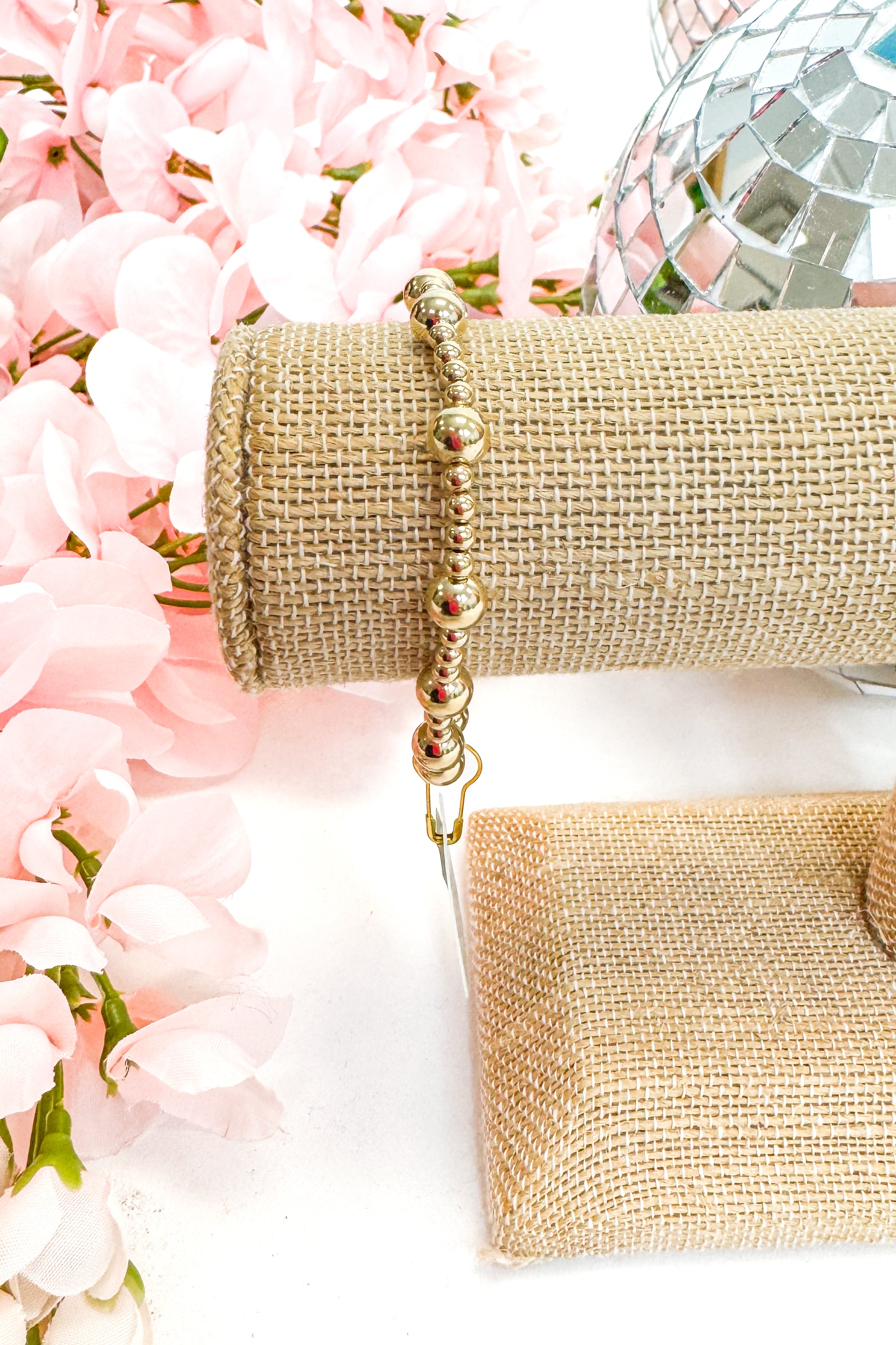 gold beaded bracelet against a pink floral background