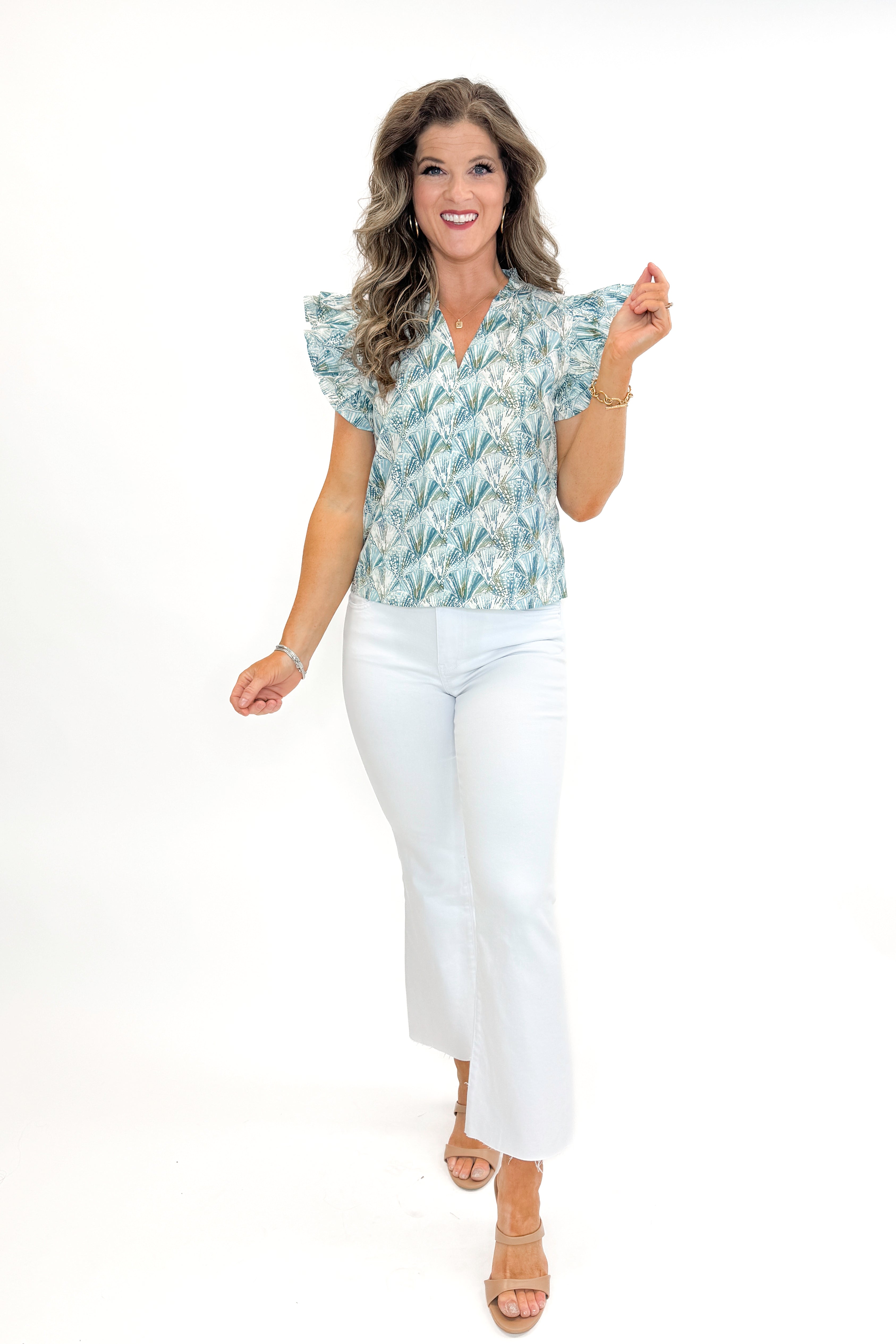 Front view of woman wearing Teal Shell Printed Flutter Sleeve Top by PINCH with jeans against white studio background.