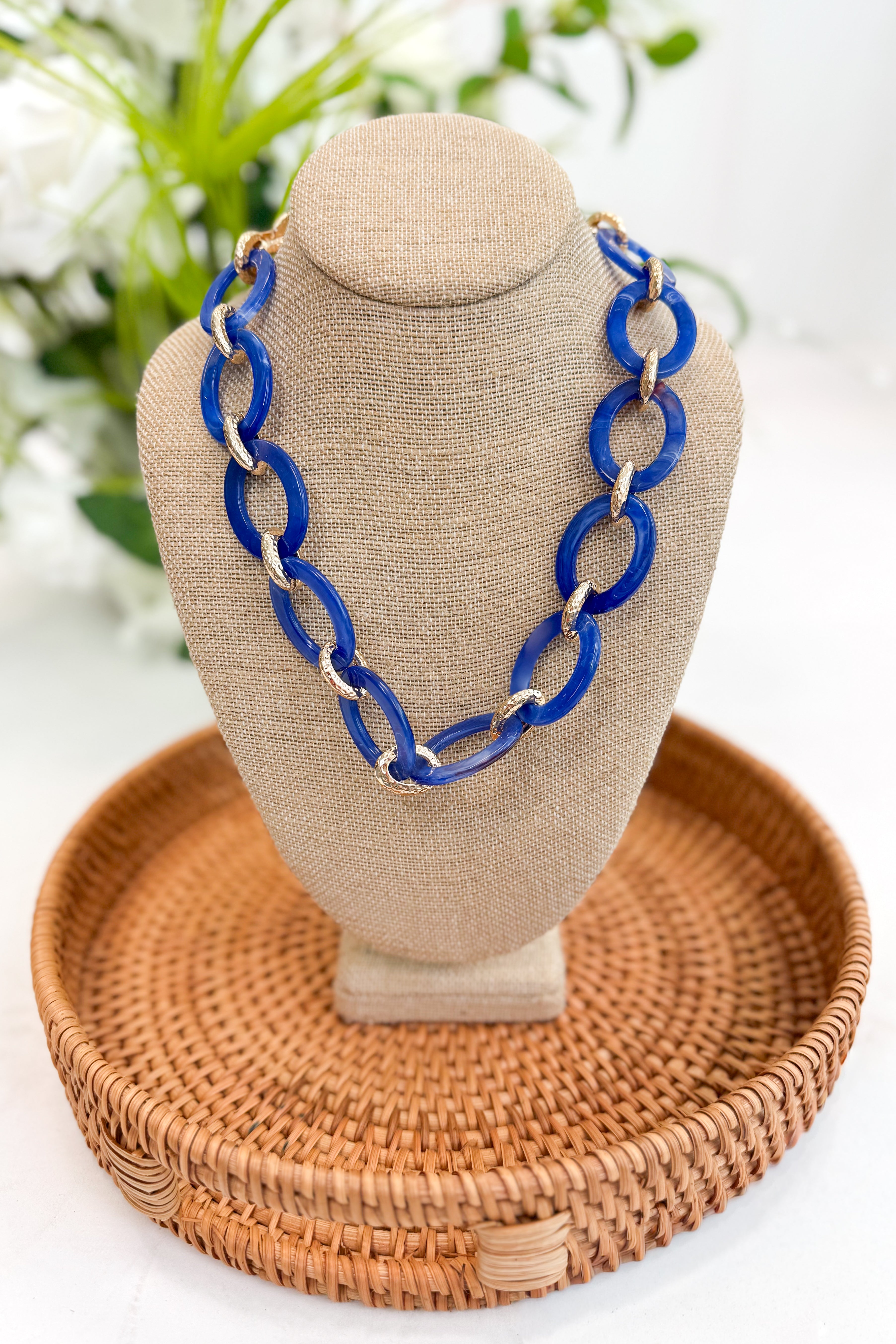 Blue chain necklace on a beige bust with a woven brown tray