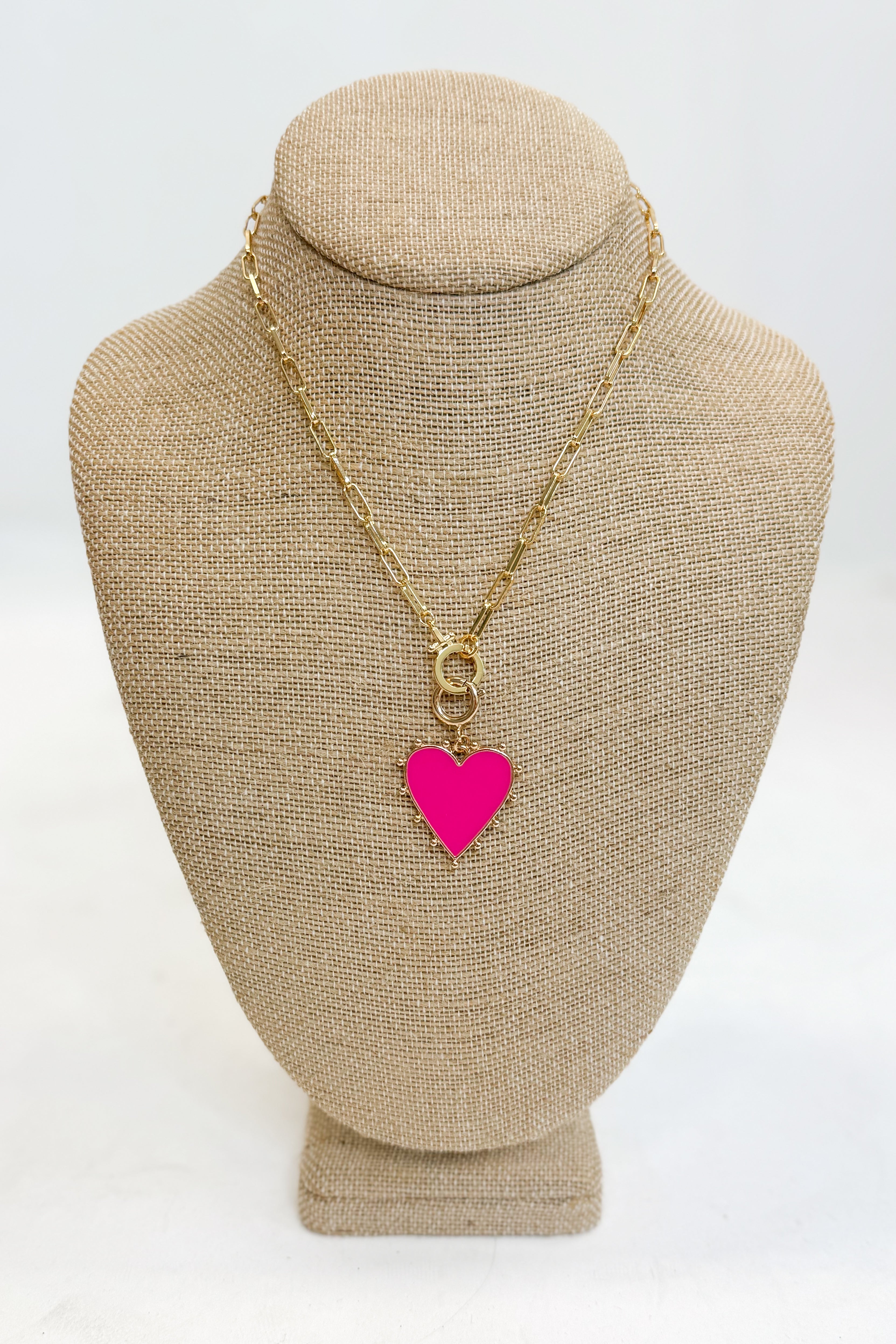 Gold necklace with a pink heart pendant on a beige bust against a white background